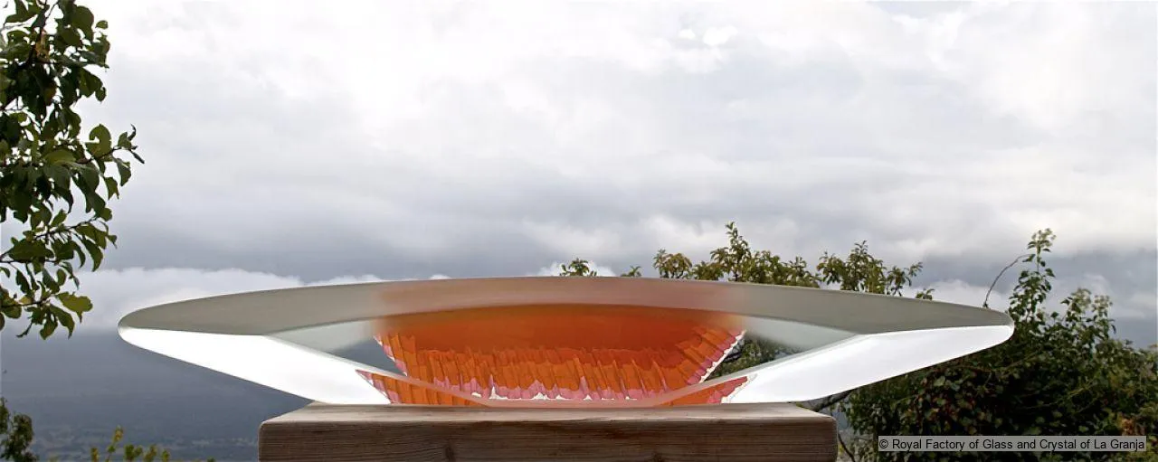 Una escultura moderna de vidrio con un cuenco naranja y alas transparentes sobre una base de madera