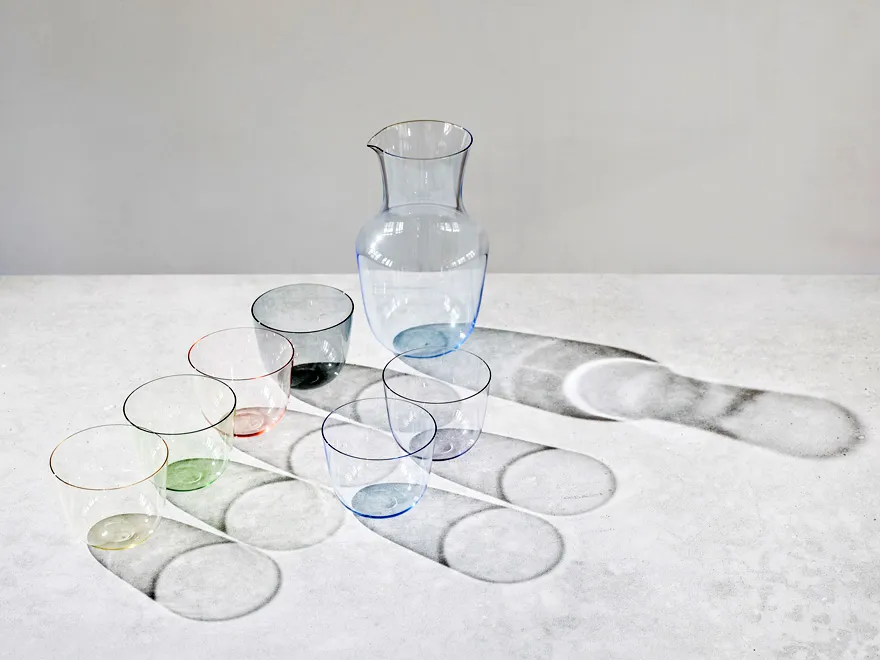 carafas y vasos de vidrio de colores dispuestos sobre una superficie blanca