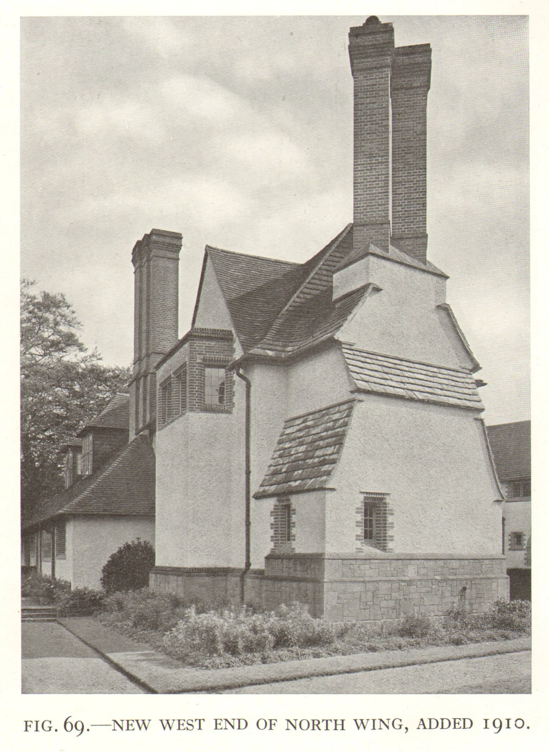 Fotografía en blanco y negro del exterior de Goddards que muestra el extremo oeste del ala norte, con altas chimeneas de ladrillo, techos de tejas y paredes de revoco blanco, añadidas en 1910.