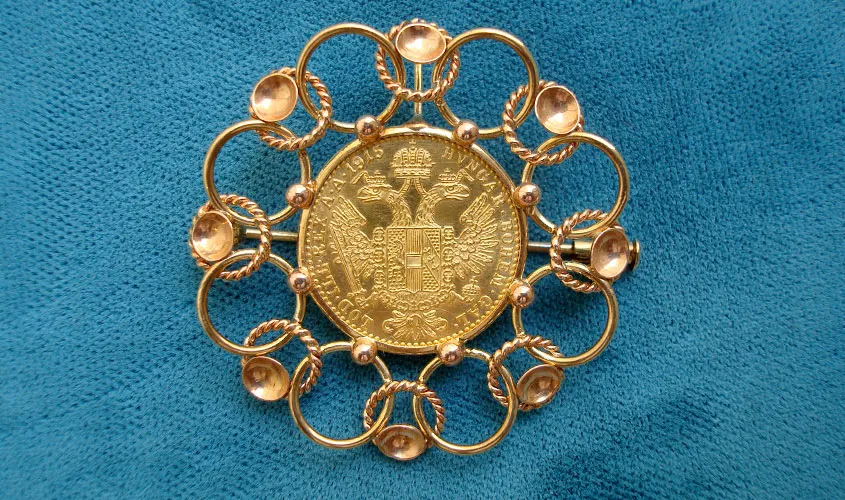 Un broche de oro con intrincados patrones circulares y un medallón central sobre una superficie azul