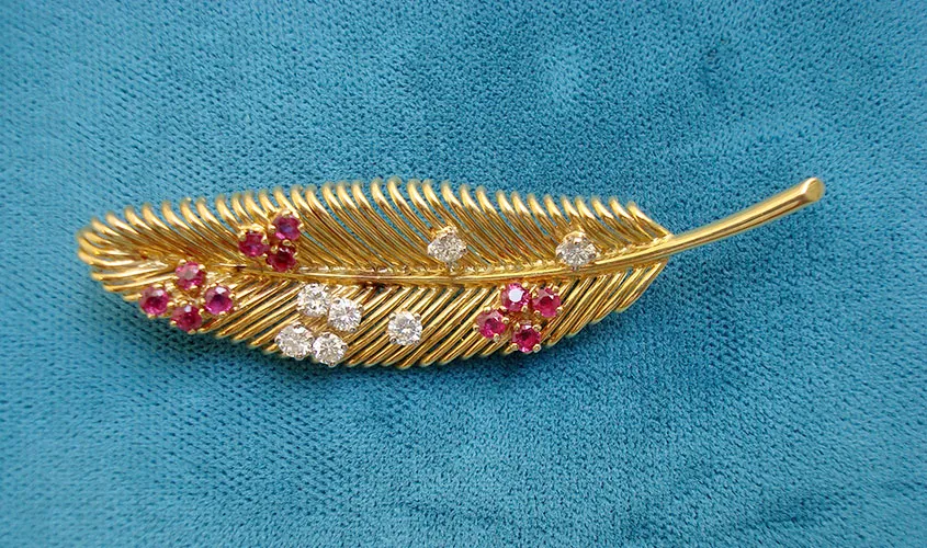 broche de plumas doradas con rubíes y diamantes sobre tela verde azulado