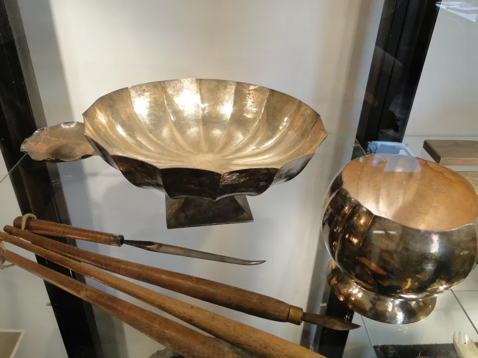 un cuenco de metal martillado y herramientas con mangos de madera en una vitrina de cristal