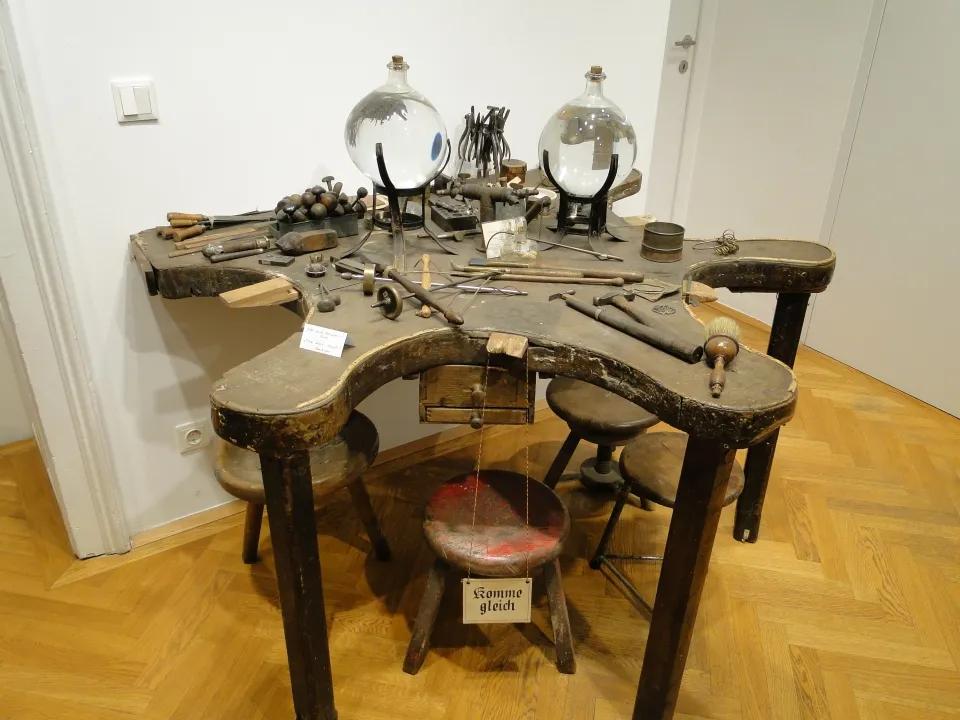 Un banco de trabajo de madera con herramientas y objetos cubiertos de vidrio en una vitrina de museo