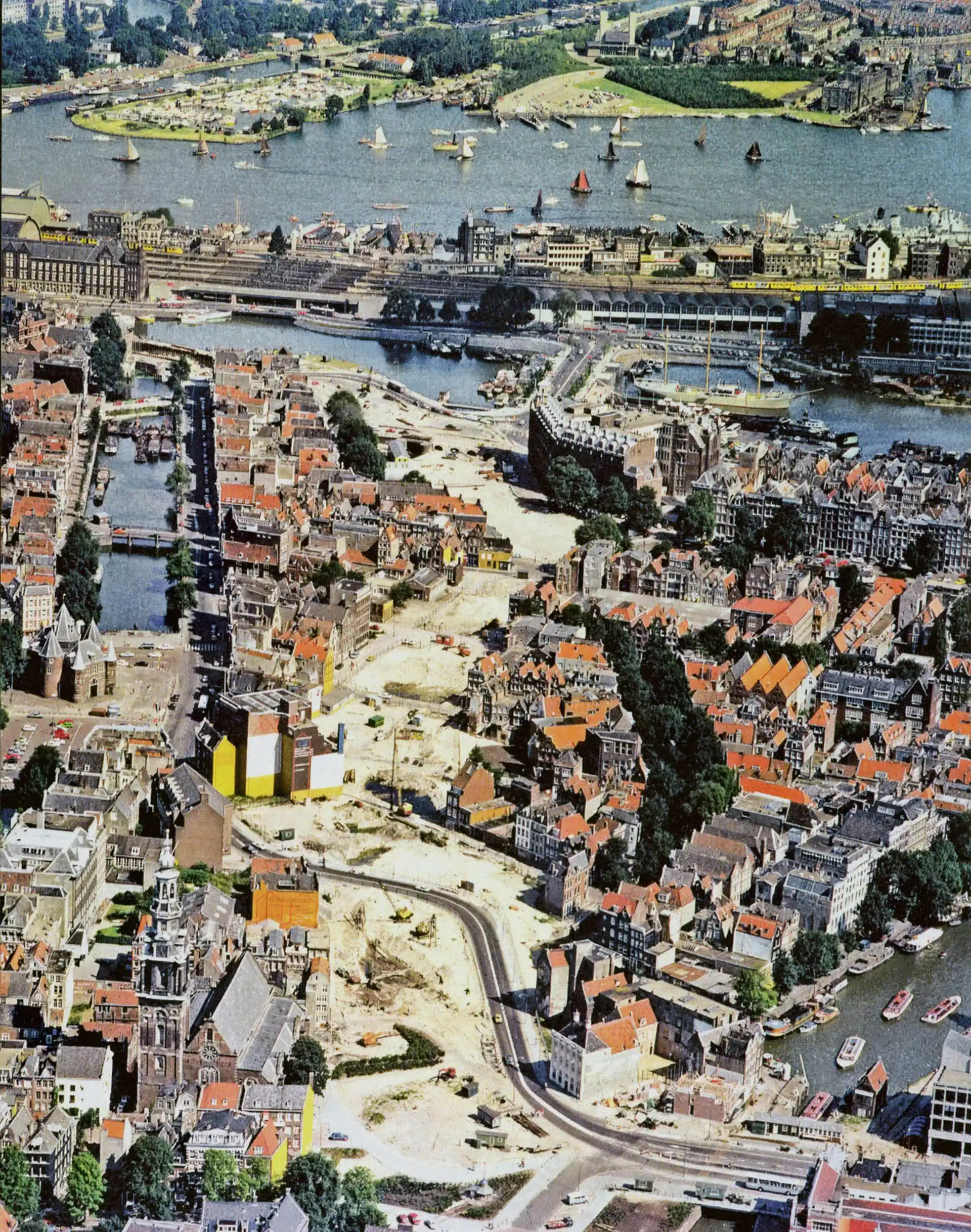 Ilustracja lotnicza historycznego pierścienia kanałów Amsterdamu z budynkami z czerwonymi dachami, drogami wodnymi i łodziami, ukazująca unikalny układ urbanistyczny miasta.