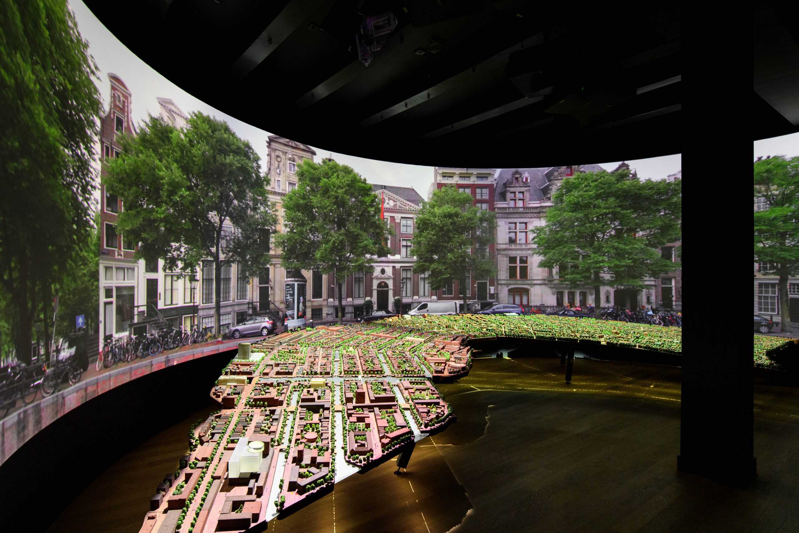 Proyección curva que muestra una escena de canales de Ámsterdam con un modelo detallado del sistema de canales en primer plano, dentro de un espacio de exhibición oscuro