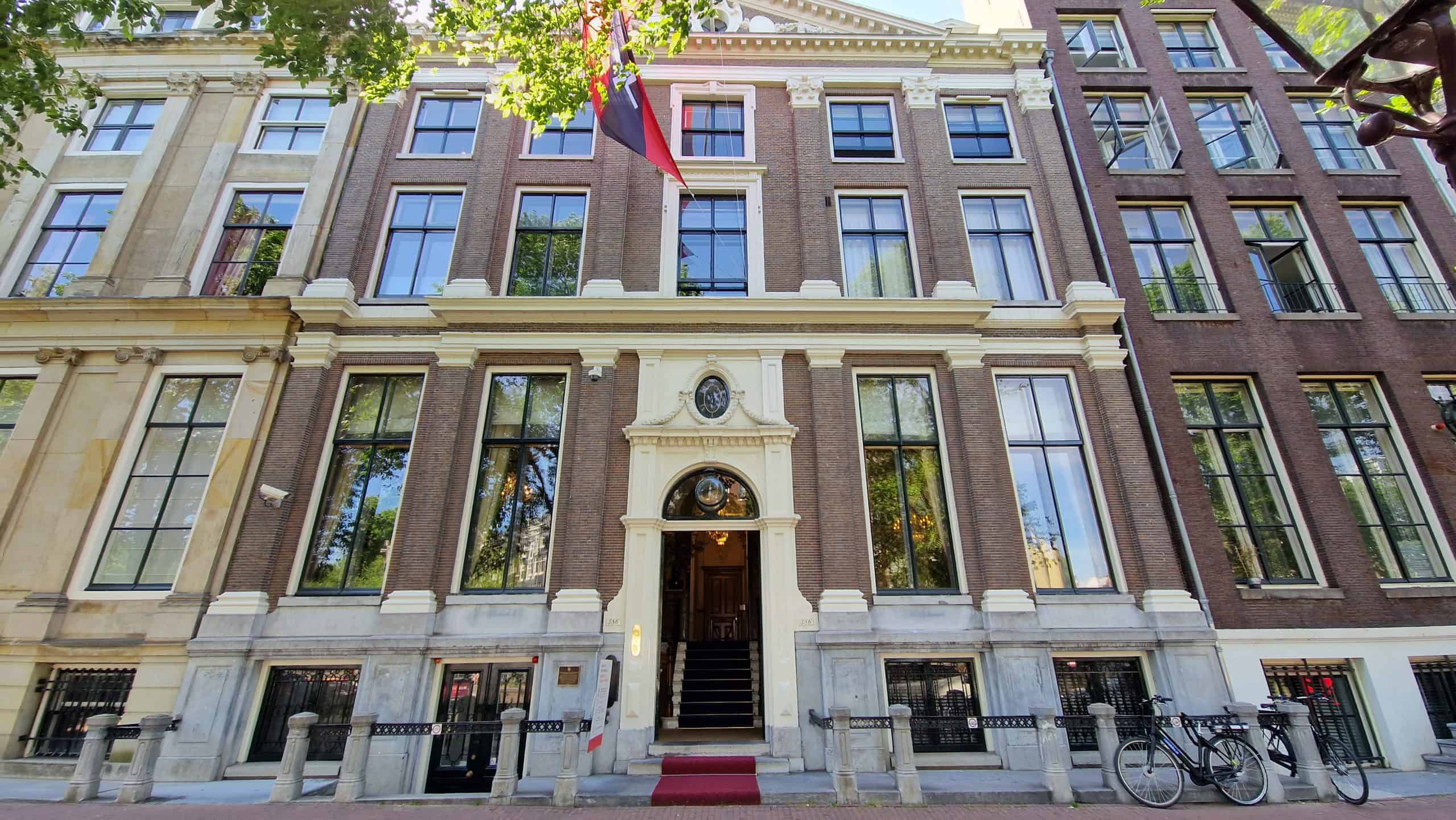 Fachada histórica de edificio de ladrillo con ventanas altas, entrada central con alfombra roja y bicicletas aparcadas a lo largo de la calle