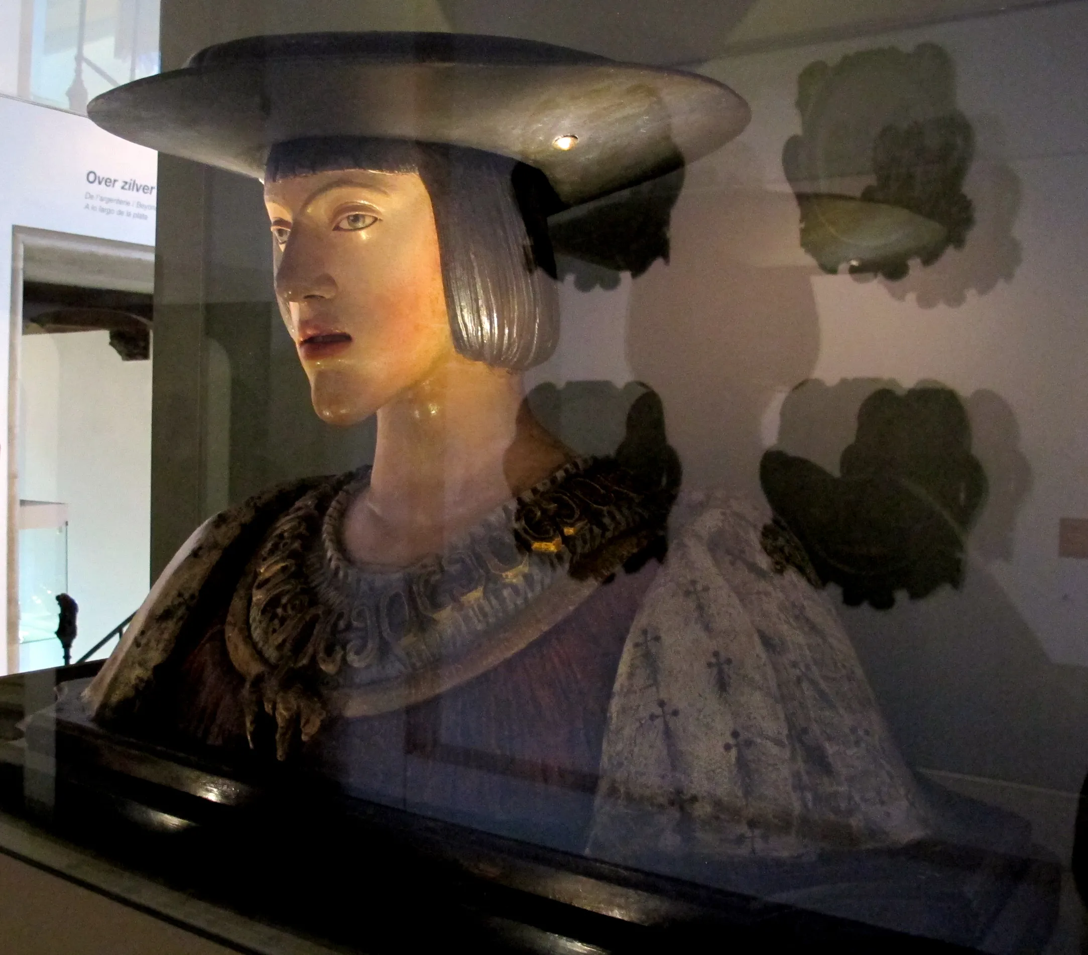 Busto de terracota de un hombre con sombrero de ala ancha y cuello ornamentado, expuesto en una vitrina en el Gruuthusemuseum