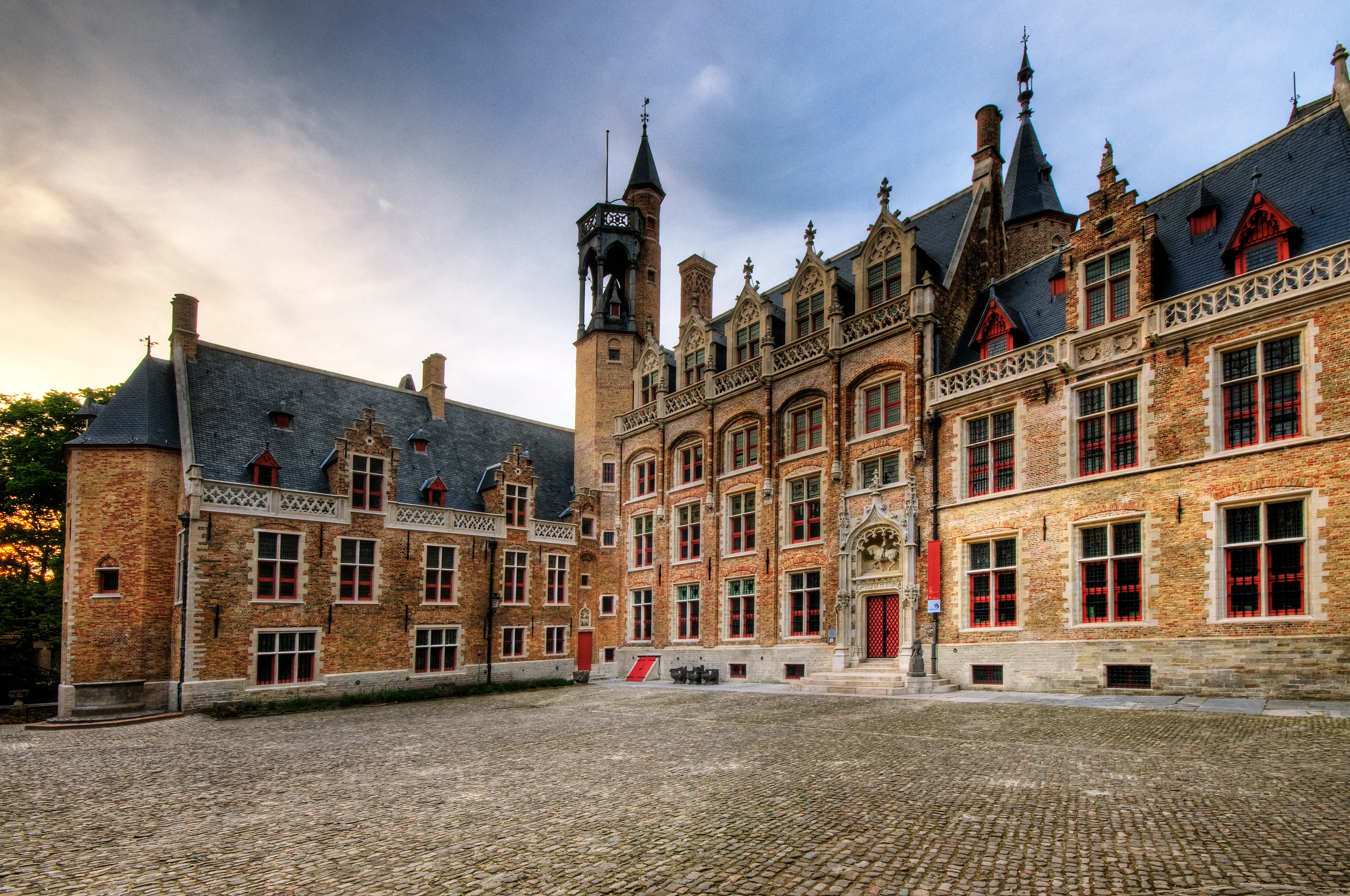 Vista exterior del Gruuthusemuseum, un histórico palacio de ladrillo con una torre de reloj, ventanas góticas y un patio empedrado bajo un cielo espectacular