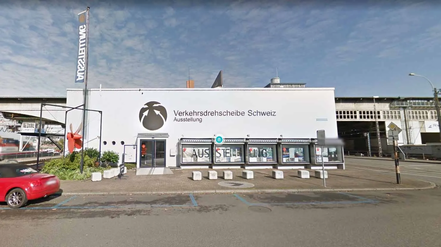 Witte gevel van een gebouw met het bord 'Verkehrsdrehscheibe Schweiz Ausstellung' en een vlag van het Hafenmuseum, met vitrines aan de buitenkant