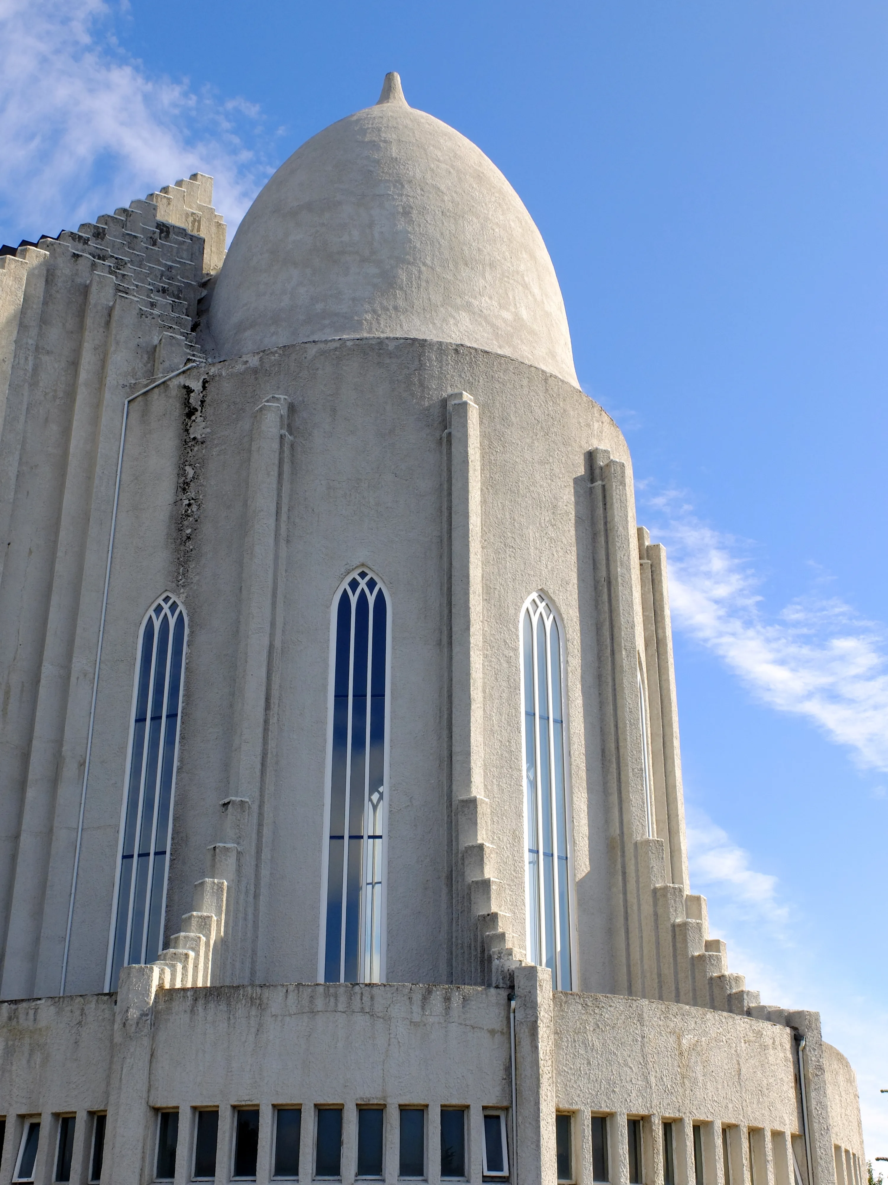 Laagstandpunt van de betonnen koepel en de op basalt geïnspireerde zuilen van Hallgrímskirkja met hoge, smalle boogramen tegen een blauwe lucht