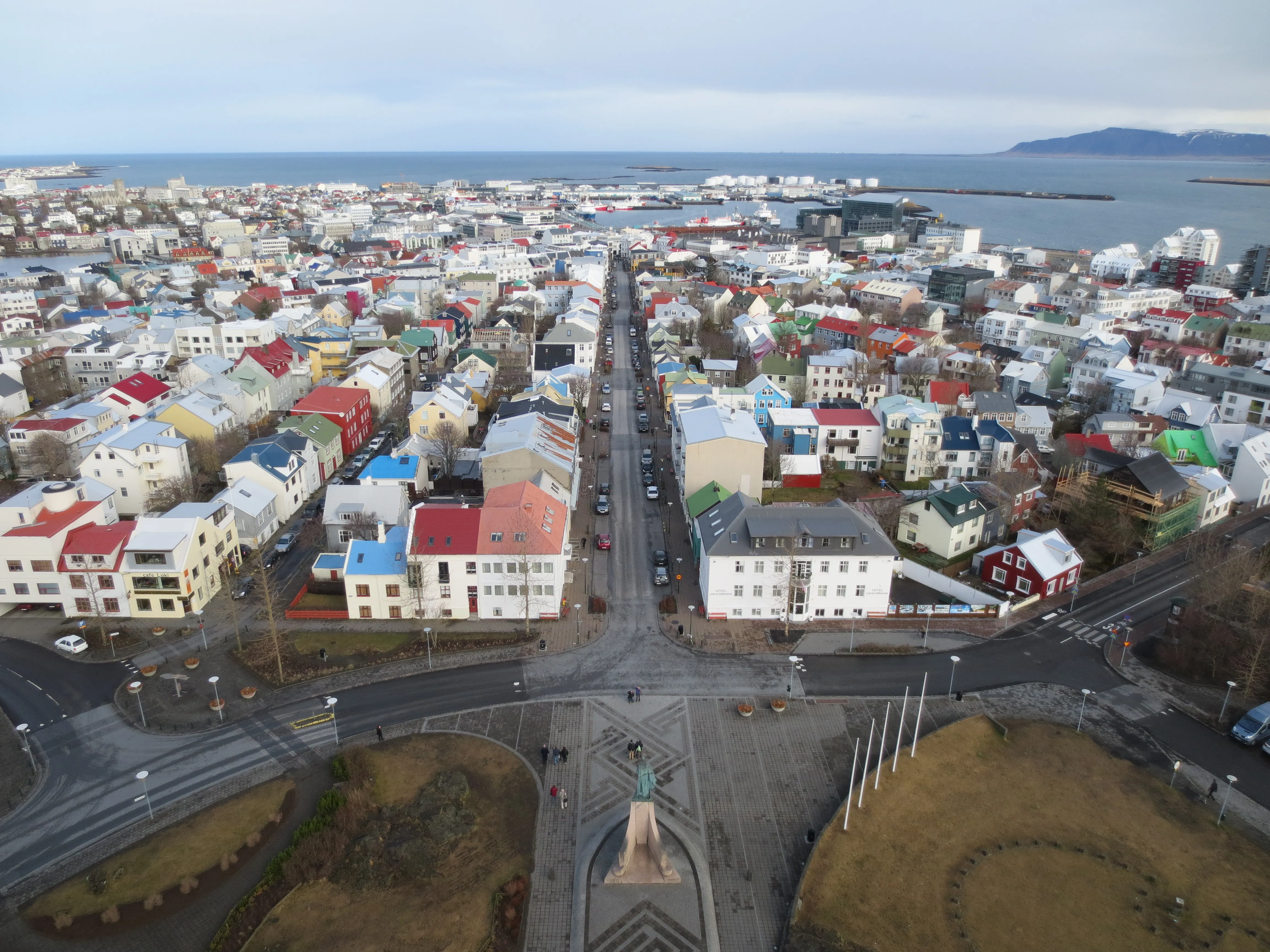 Luchtfoto van Reykjavík met een raster van kleurrijke daken, een lange rechte straat die naar de haven en de zee leidt, met het standbeeld van Leif Erikson zichtbaar beneden aan de voet van Hallgrímskirkja.