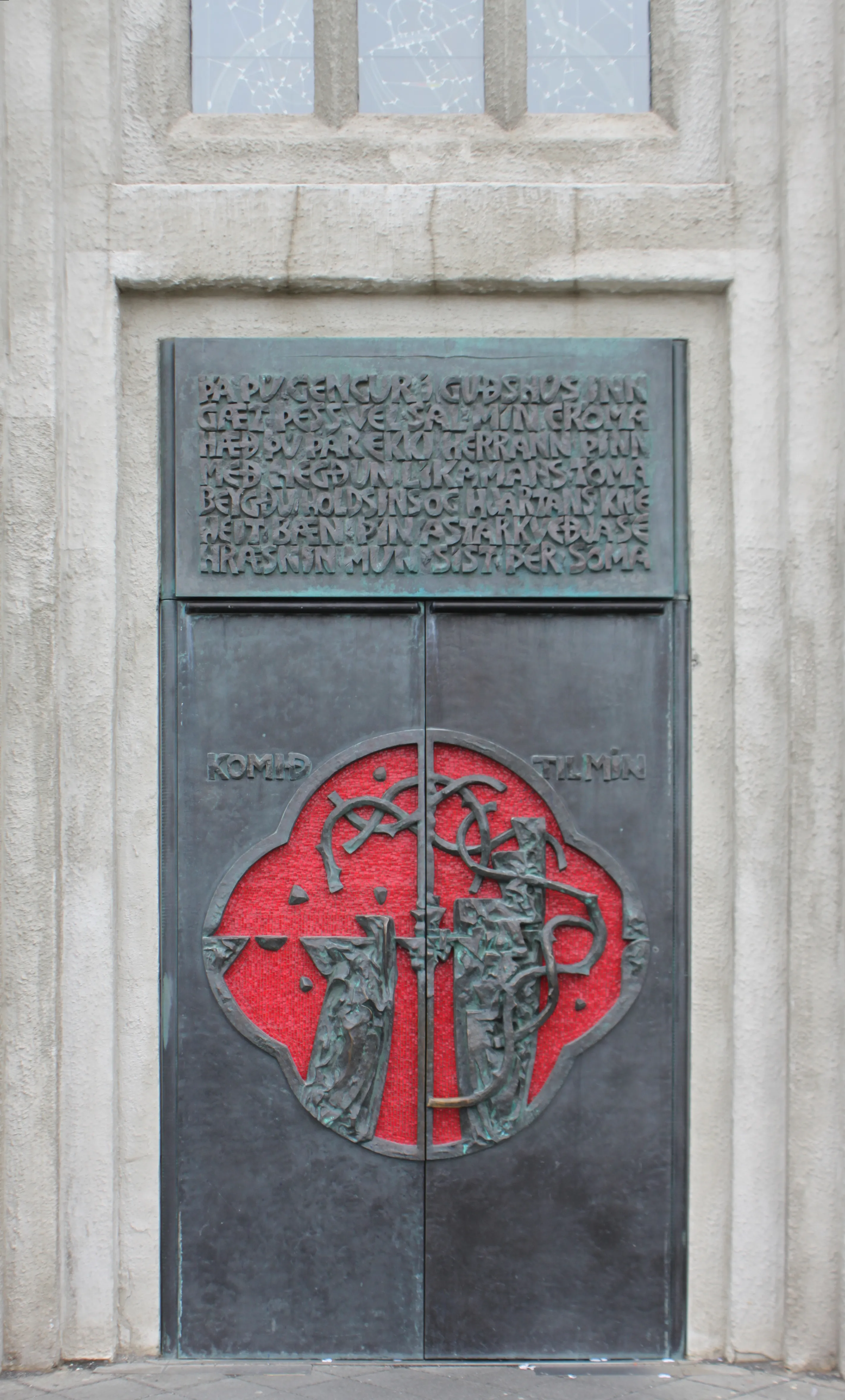 Bronzen voordeur van de Hallgrímskirkja-kerk met rood cirkelvormig reliëf met figuren en een IJslandse inscriptie erboven