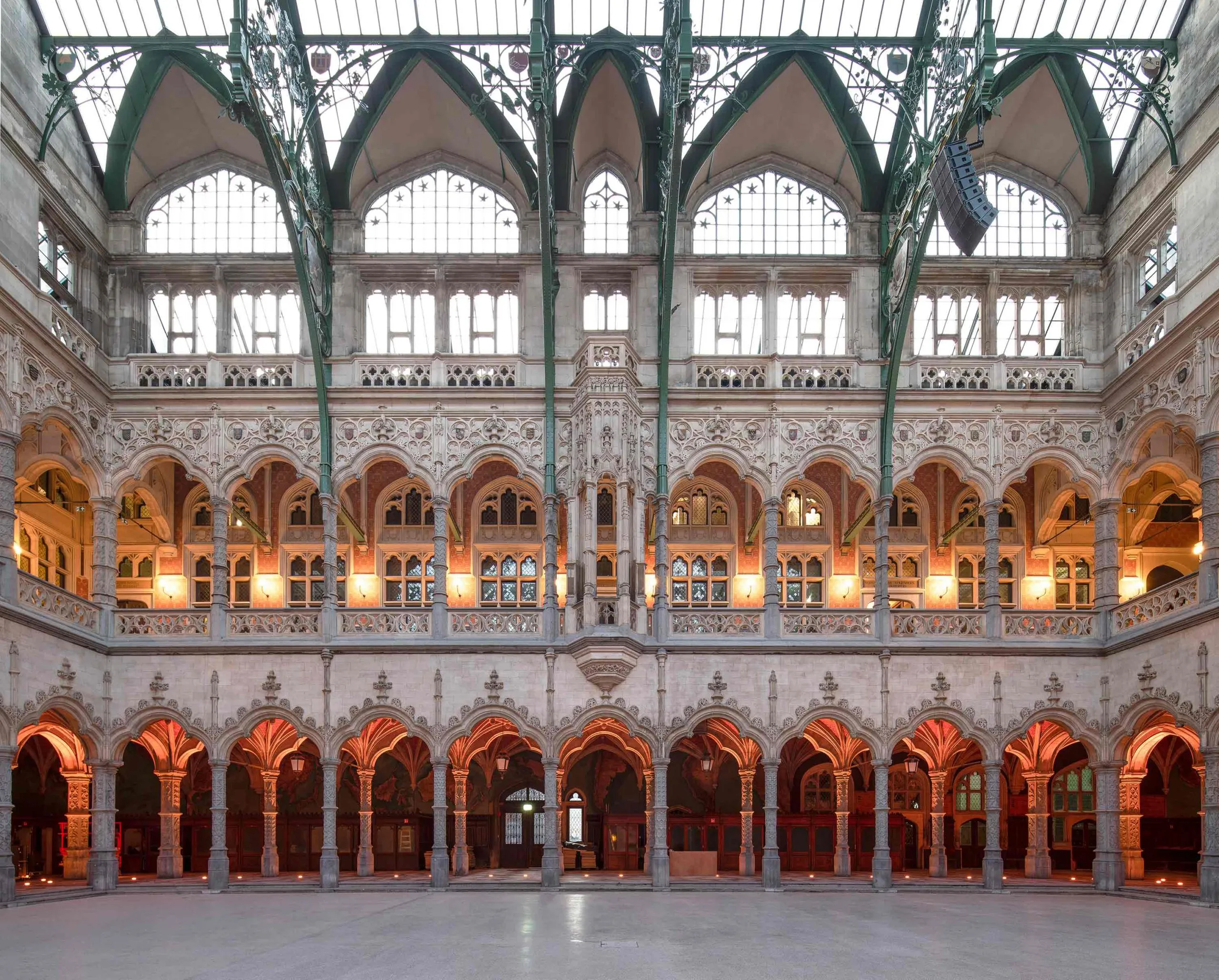 Vista interior amplia del patio cubierto de la neogótica Handelsbeurs Antwerpen, que muestra galerías arqueadas ornamentadas con arcos apuntados, detalles en piedra y un techo de cristal.