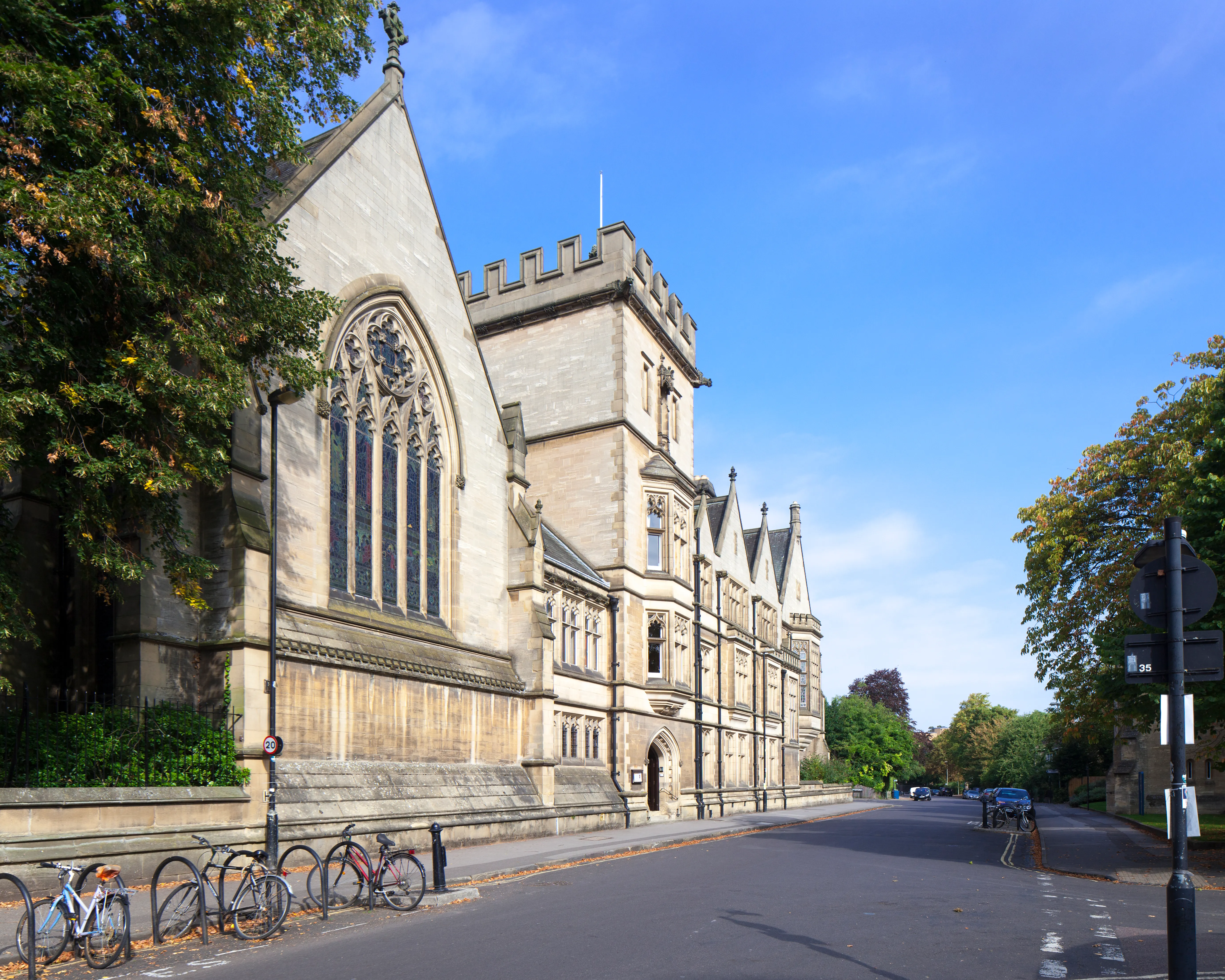 Buitenaanzicht van Harris Manchester College vanaf Mansfield Road, met de kapel met een groot gotisch boogvenster en de stenen gevel van het gebouw, met fietsen geparkeerd langs de straat.