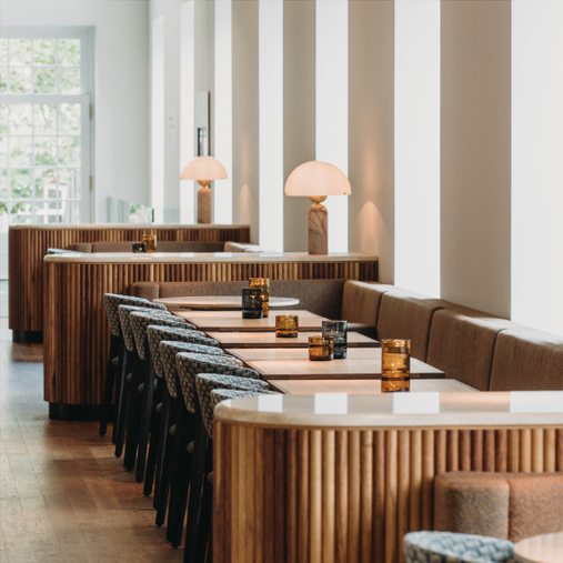 Modern interior with wooden tables, patterned chairs, and tall lamps in a bright room with large windows