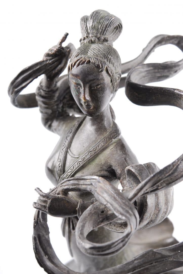 Bronze statue of a female figure with flowing ribbons, wearing traditional attire, posed with one hand raised