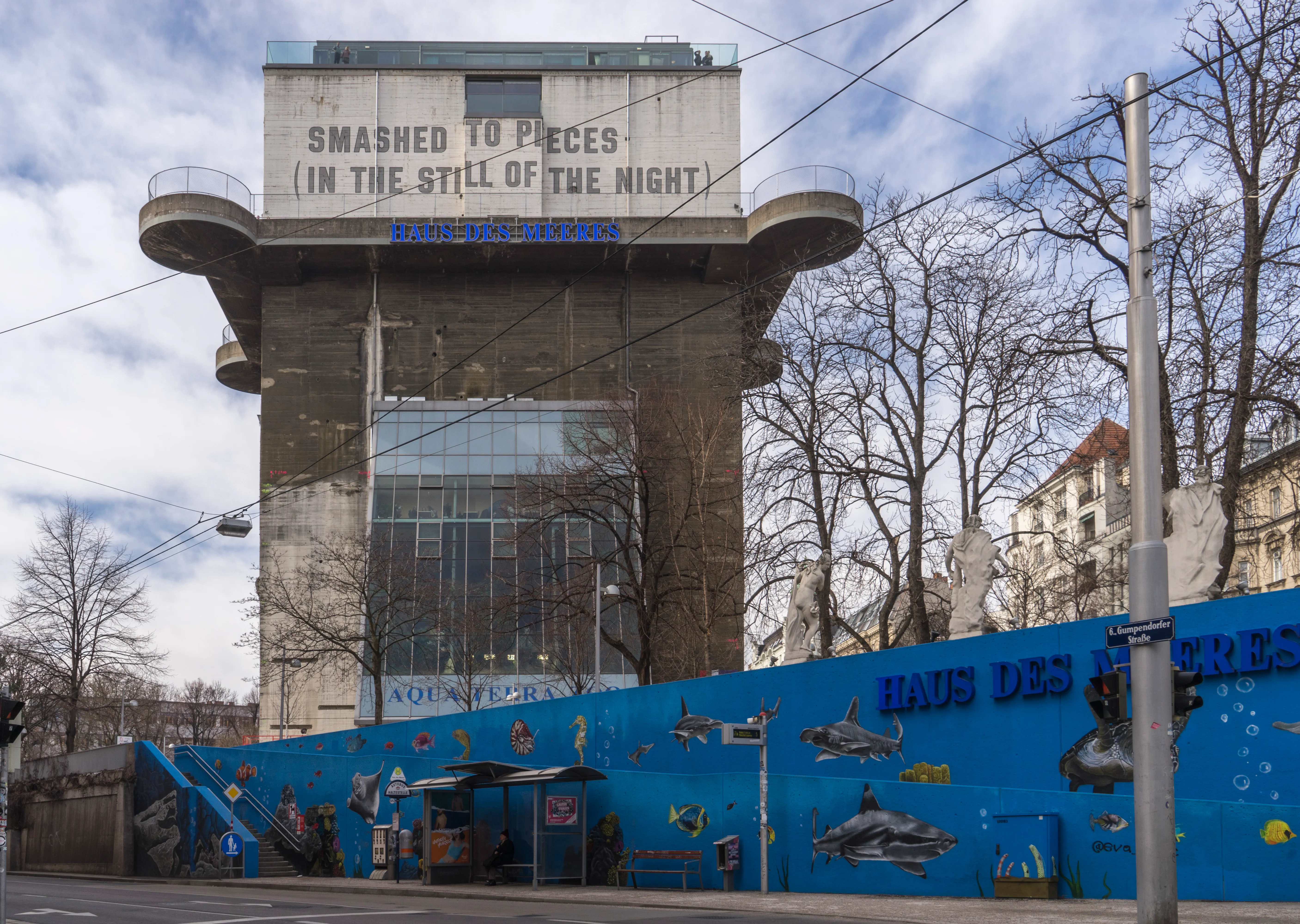 A large concrete flak tower with a sign reading 'SMASHED TO PIECES (IN THE STILL OF THE NIGHT)' and a blue wall with marine animal illustrations at its base