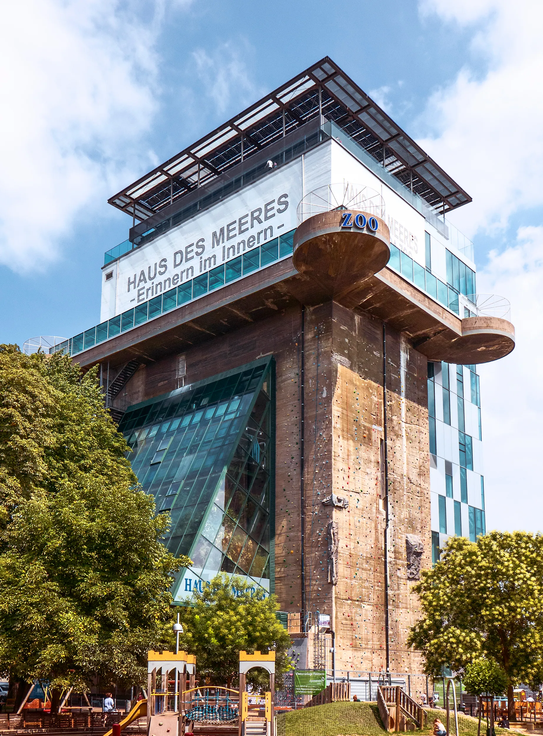 Een grote betonnen flak-toren met moderne glazen uitbreidingen en een bord met de tekst 'HAUS DES MEERES -Erinnern im Innern-'.