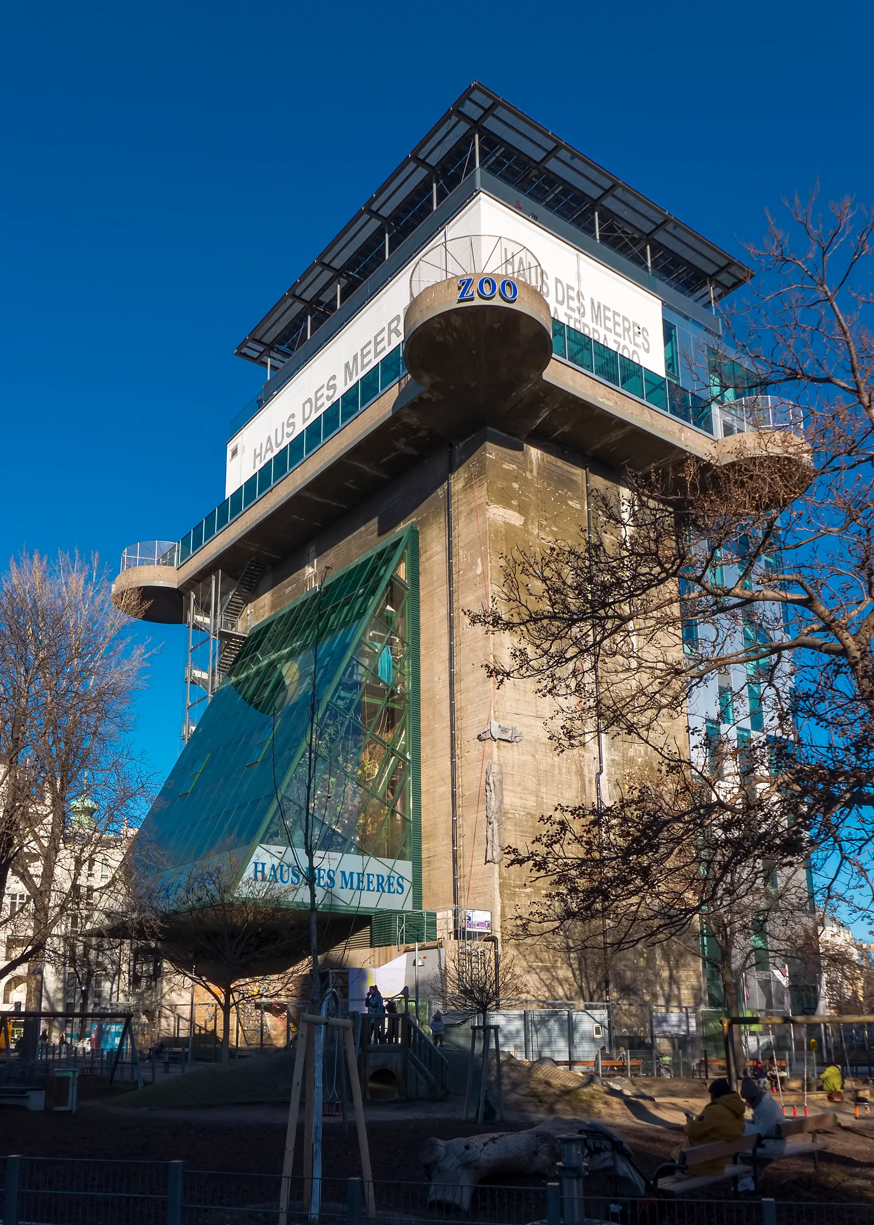Een hoge betonnen flak toren met 'Haus des Meeres' en 'Zoo' belettering, voorzien van grote glazen panelen en een modern observatiedek onder een helderblauwe hemel.