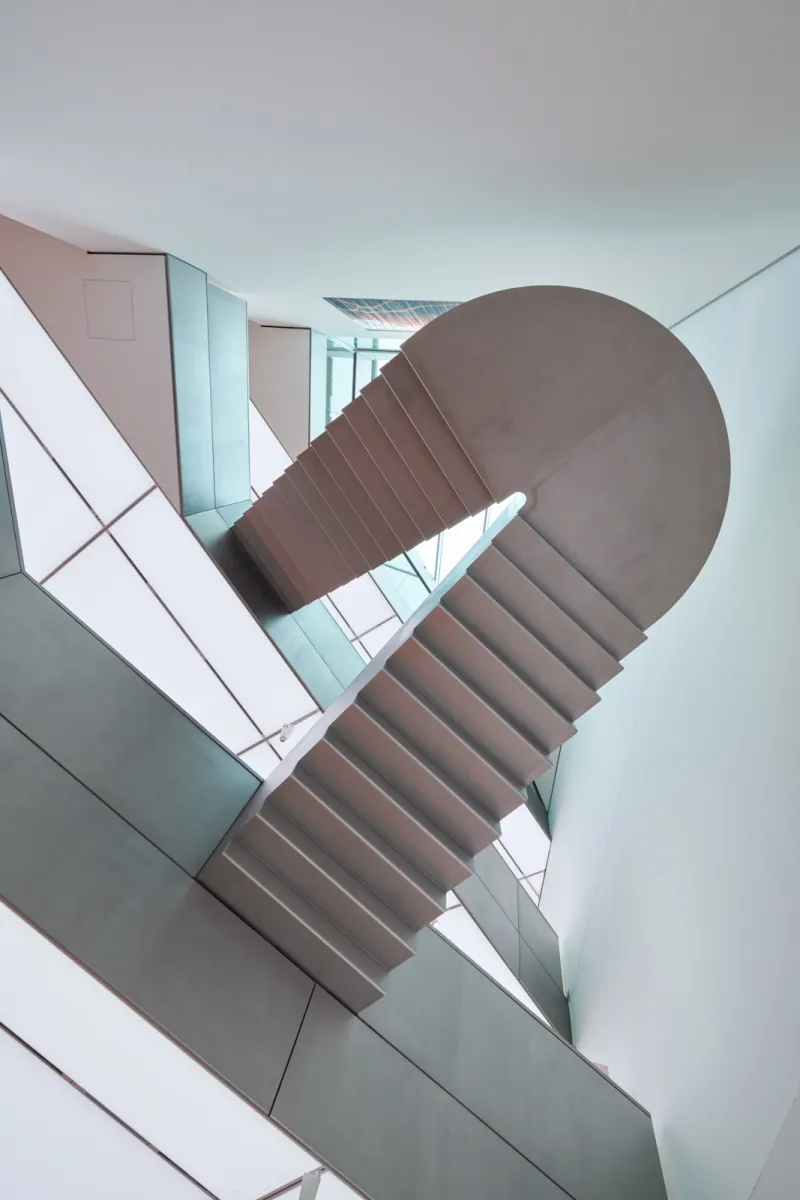 A modern spiral staircase with curved concrete steps and geometric white and pastel-colored walls