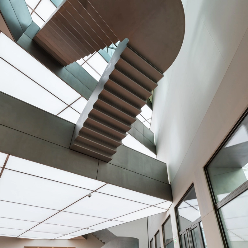 Modern staircase with curved wooden steps and glass railings under skylights