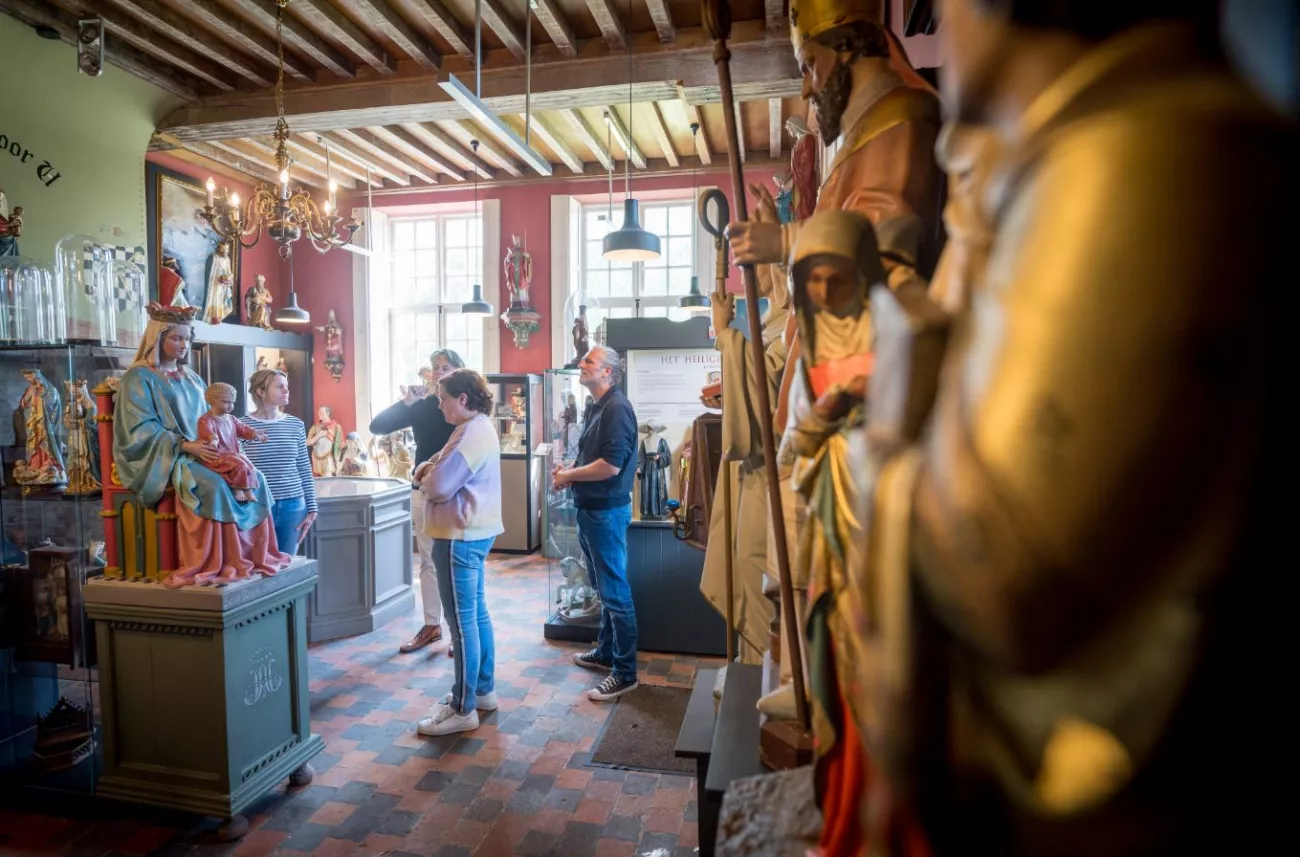 Visitantes observando estatuas religiosas dentro de un museo con techo de vigas de madera y suelo de ladrillo