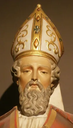 Primer plano de una estatua de un santo barbudo que lleva una mitra ornamentada en blanco y oro con volutas decorativas y detalles que parecen piedras preciosas