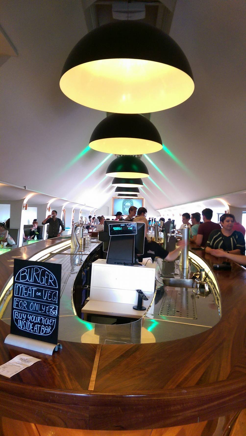 curved wooden bar with black pendant lights and people seated at the counter
