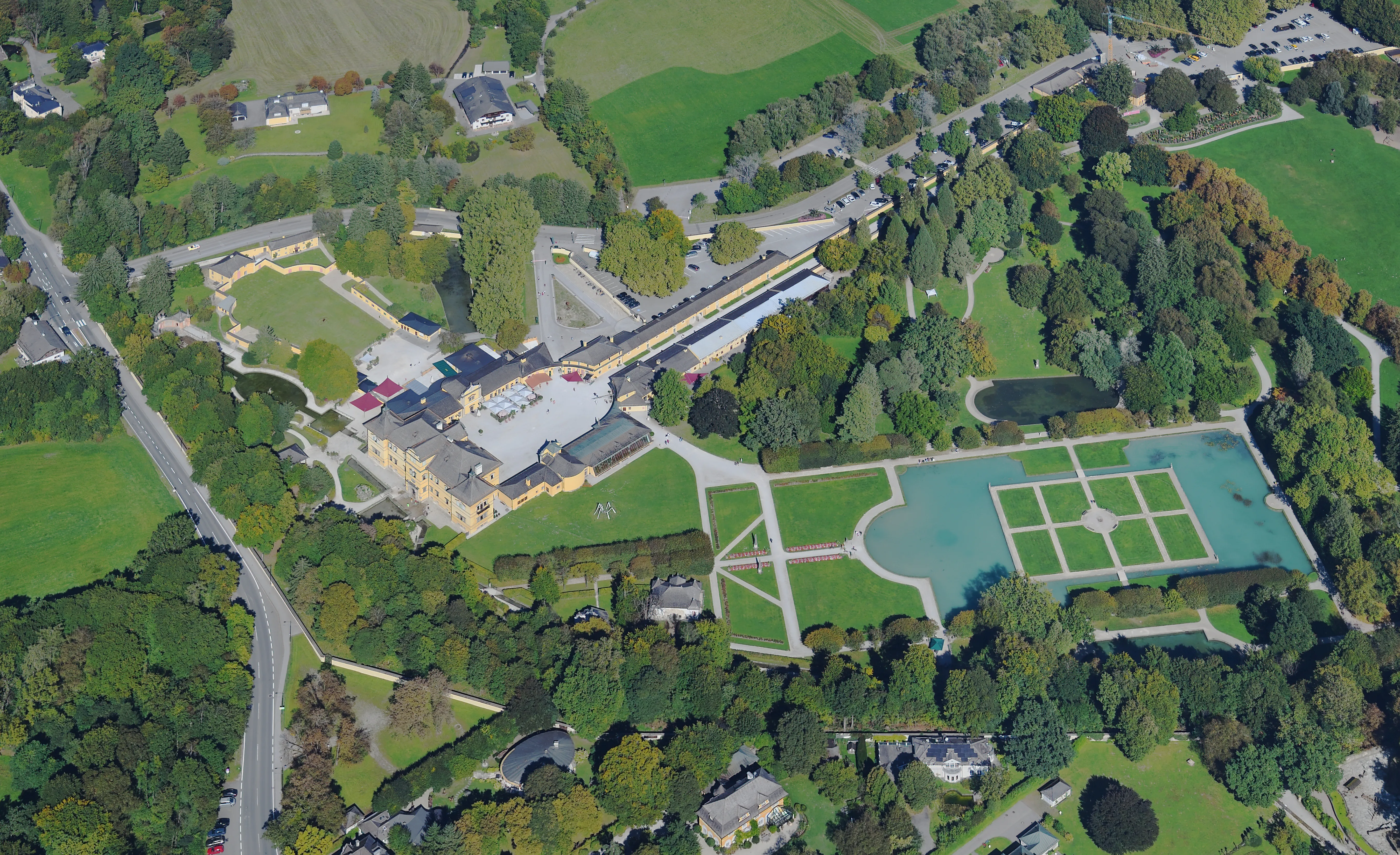 Vista aérea del Palacio de Hellbrunn que muestra el edificio principal, los jardines formales con un gran estanque rectangular y el parque y los árboles circundantes.