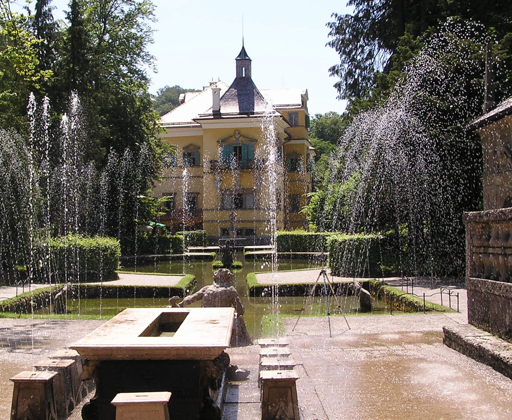 El palacio amarillo de Hellbrunn visto a través de los chorros de agua activos de las fuentes ornamentales en el patio del jardín.