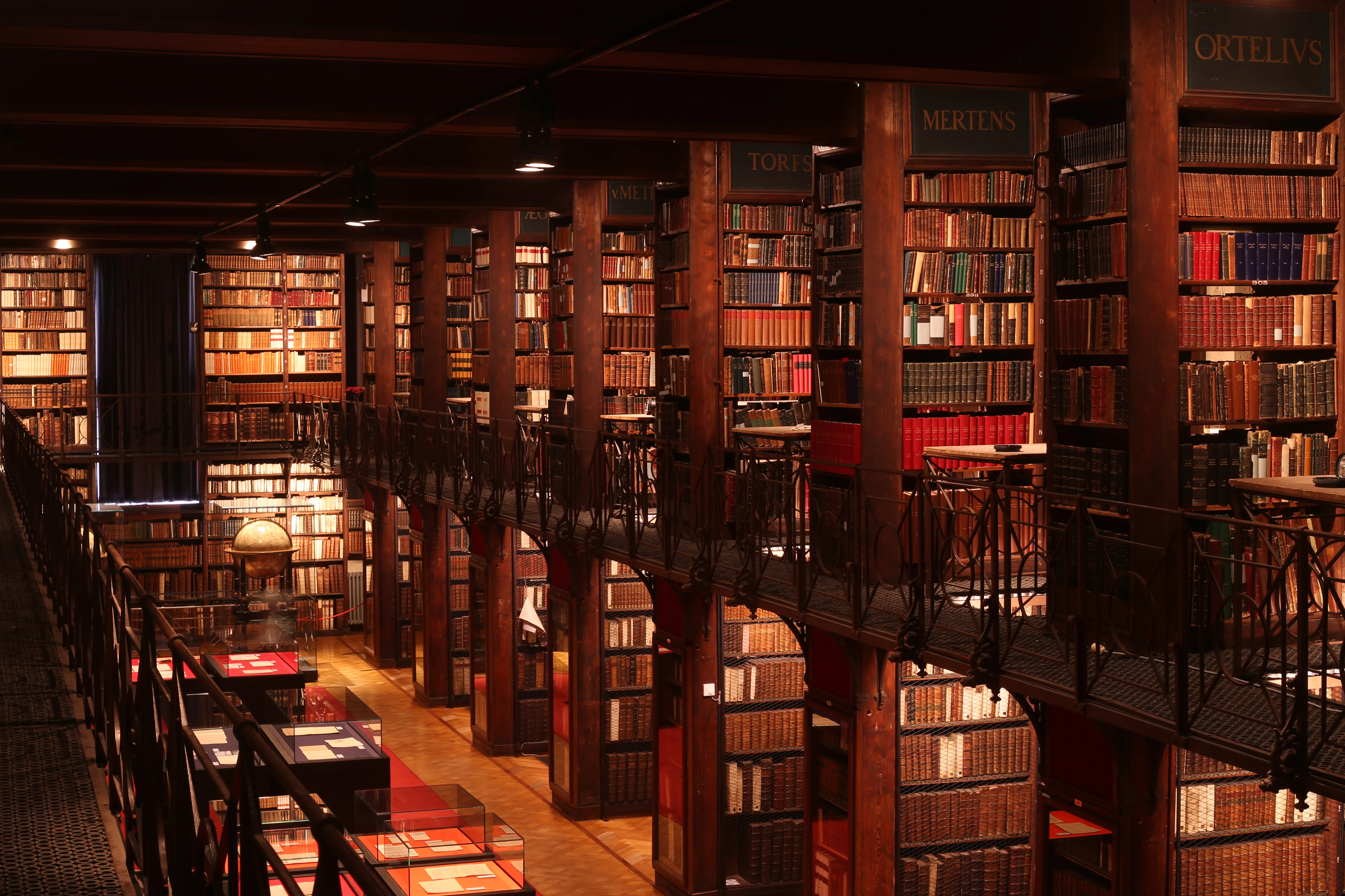 Vista interior de la Sala Nottebohm que muestra estanterías de madera de gran altura repletas de libros en varios niveles, con barandillas de hierro y una cálida iluminación ambiental