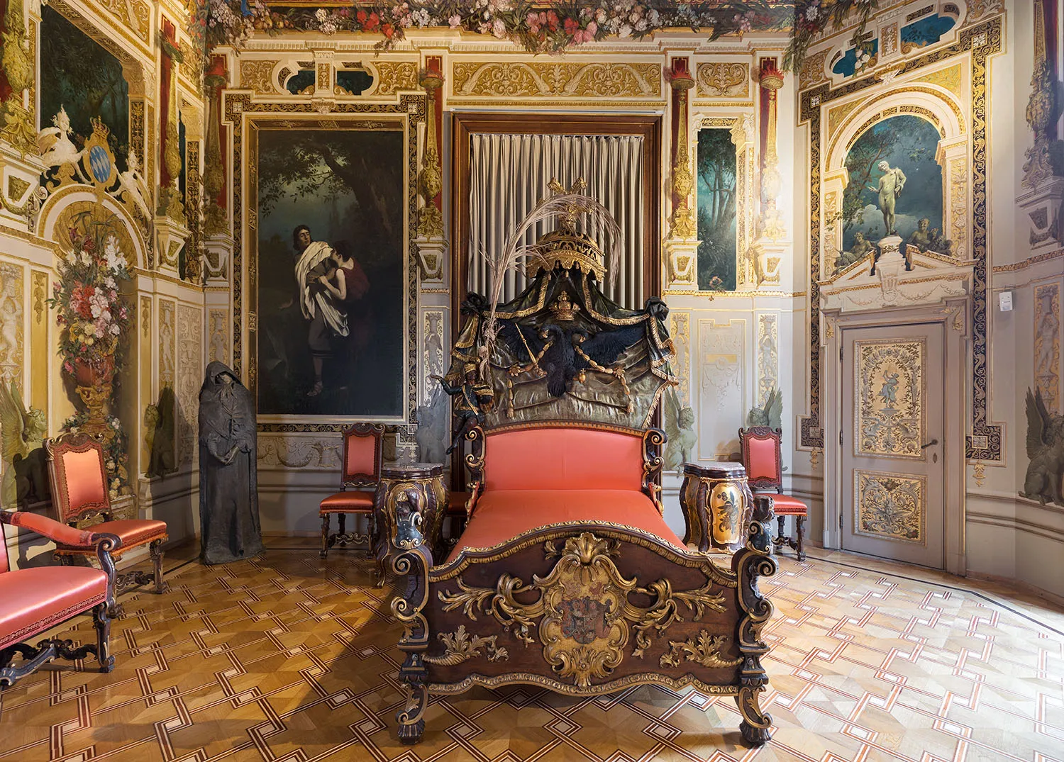 Ornate bedroom with a gilded bed, red upholstery, and frescoed walls