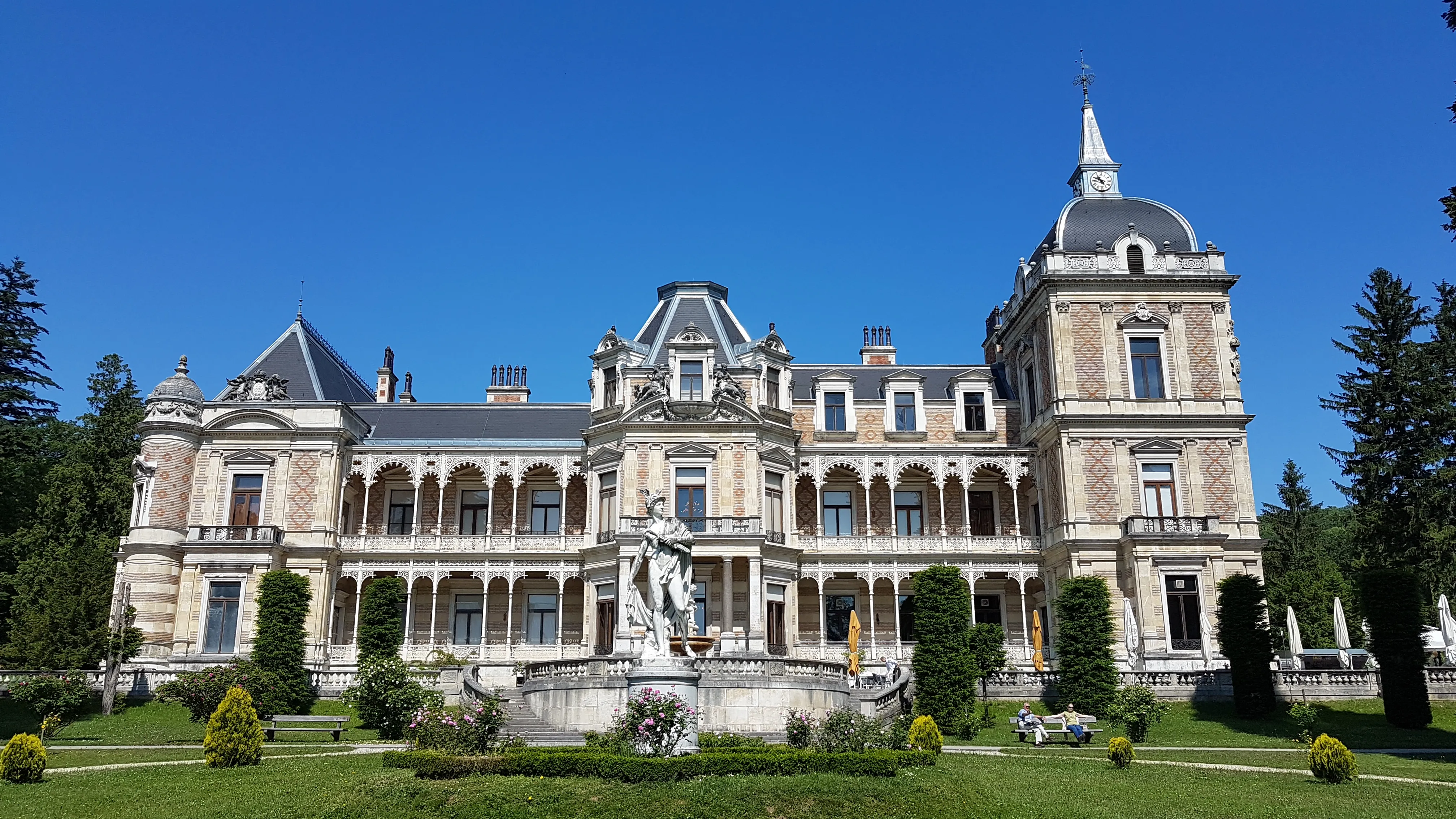 A large, ornate imperial villa with a central fountain and manicured gardens under a clear blue sky
