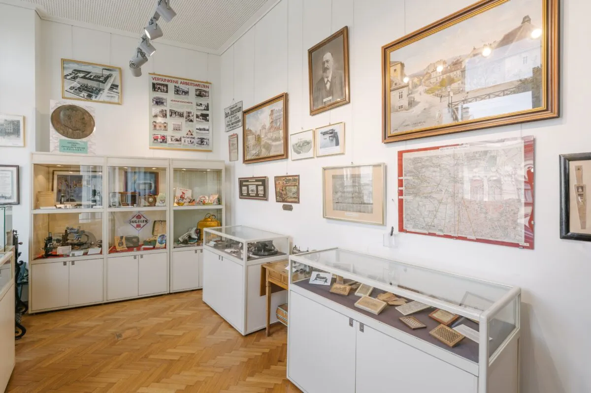 Witte vitrines met artefacten en ingelijste foto's aan witte muren in een museumgalerie