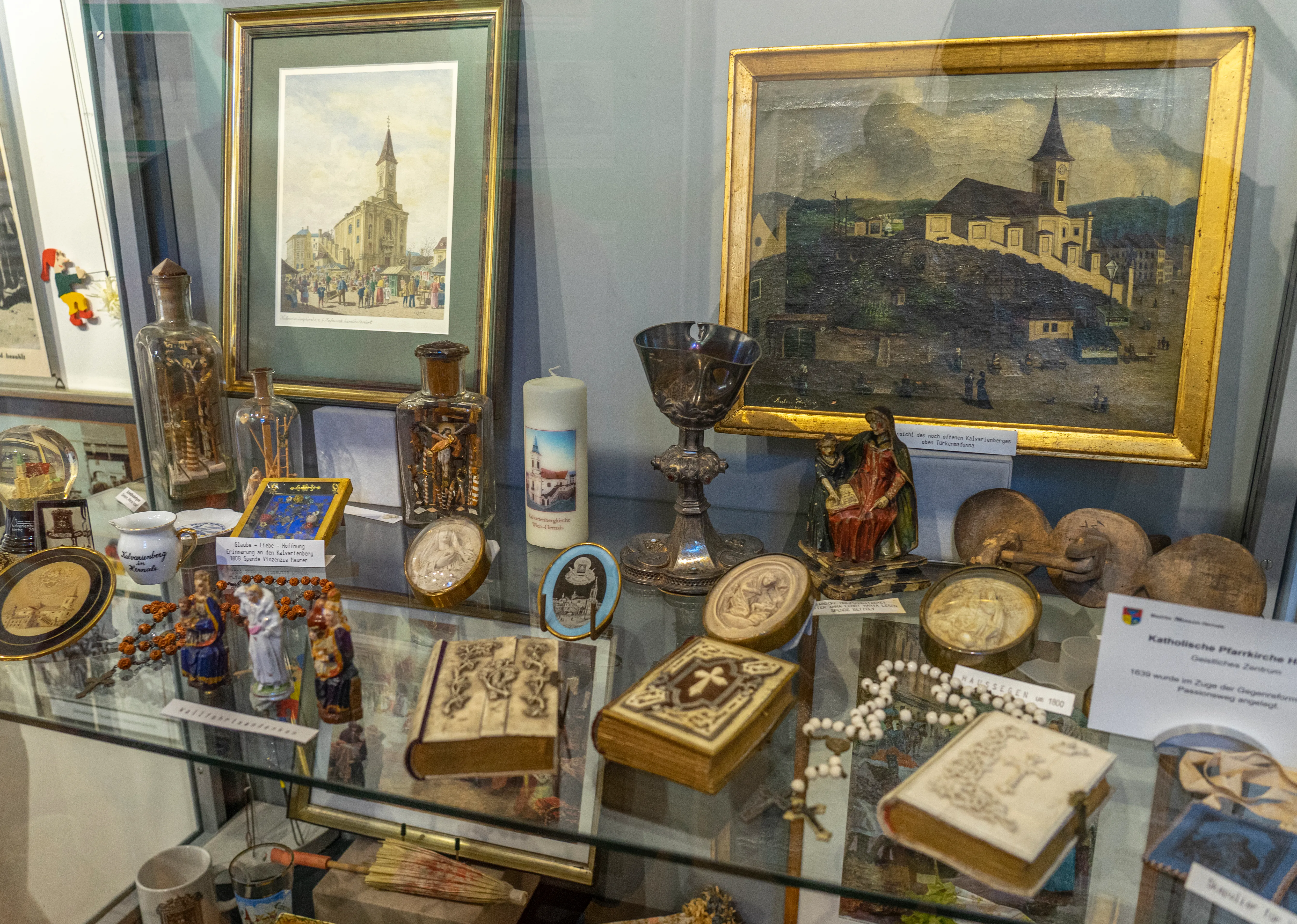 glazen vitrine gevuld met religieuze artefacten en ingelijste schilderijen