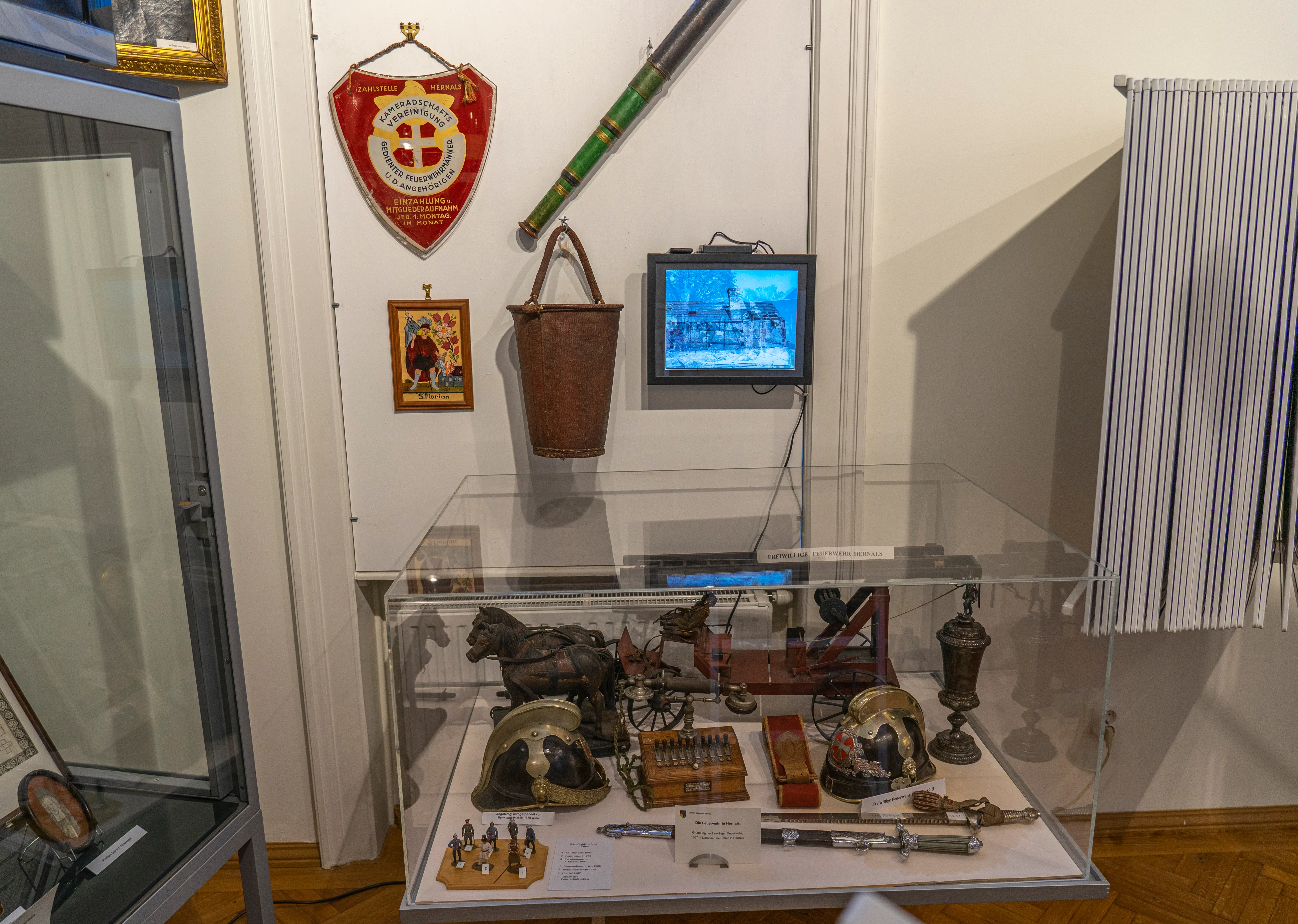 vitrina con artefactos históricos, cascos, herramientas y un escudo en la pared