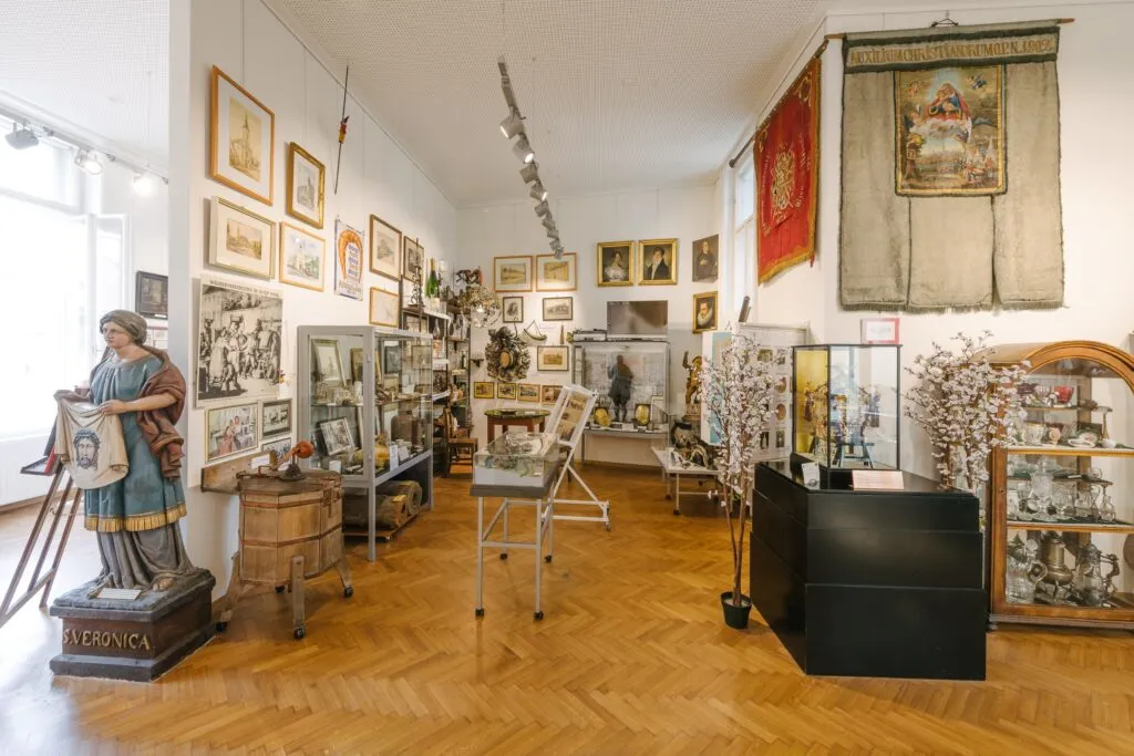 Interieur van een museumgalerij met houten vloeren, vitrines, ingelijste kunstwerken en een standbeeld