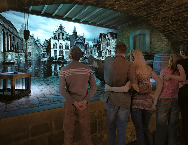 Visitantes de pie en una sala con bóveda de ladrillo observan una gran pantalla panorámica curva que muestra una escena histórica de Brujas con edificios junto al canal y calles adoquinadas.