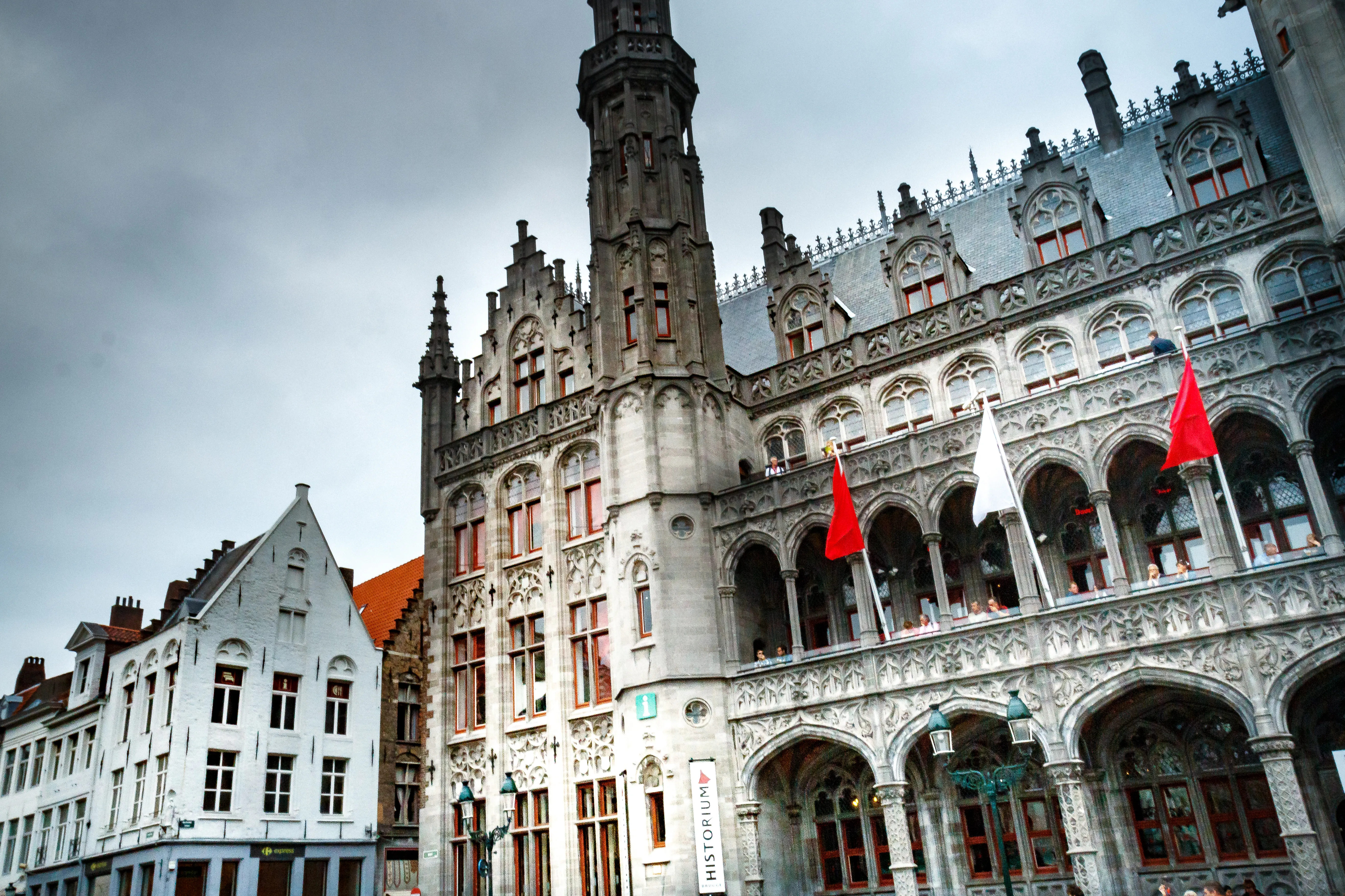 Vista exterior del histórico edificio Provinciaal Hof que alberga el Historium de Brujas, con una ornamentada fachada neogótica de ventanas arqueadas, mampostería decorativa y banderas rojas y blancas en el balcón.