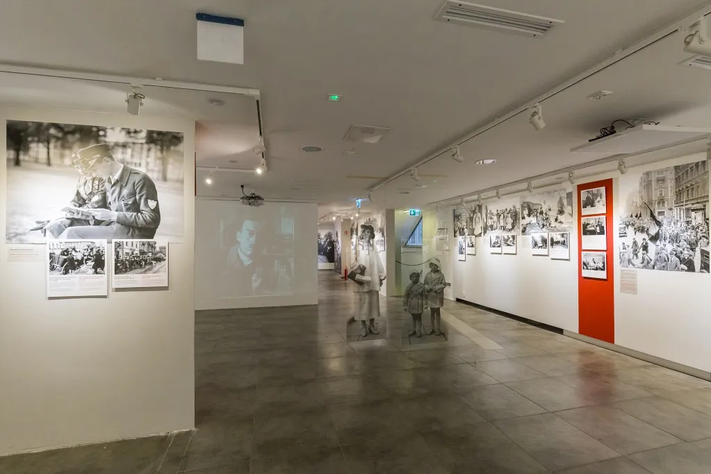tentoonstellingshal met zwart-witfoto's op witte muren en een rode deur