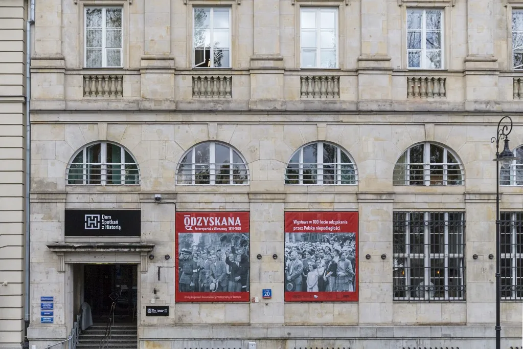 Beige stenen gebouw met boogramen en rode tentoonstellingsbanners op de gevel