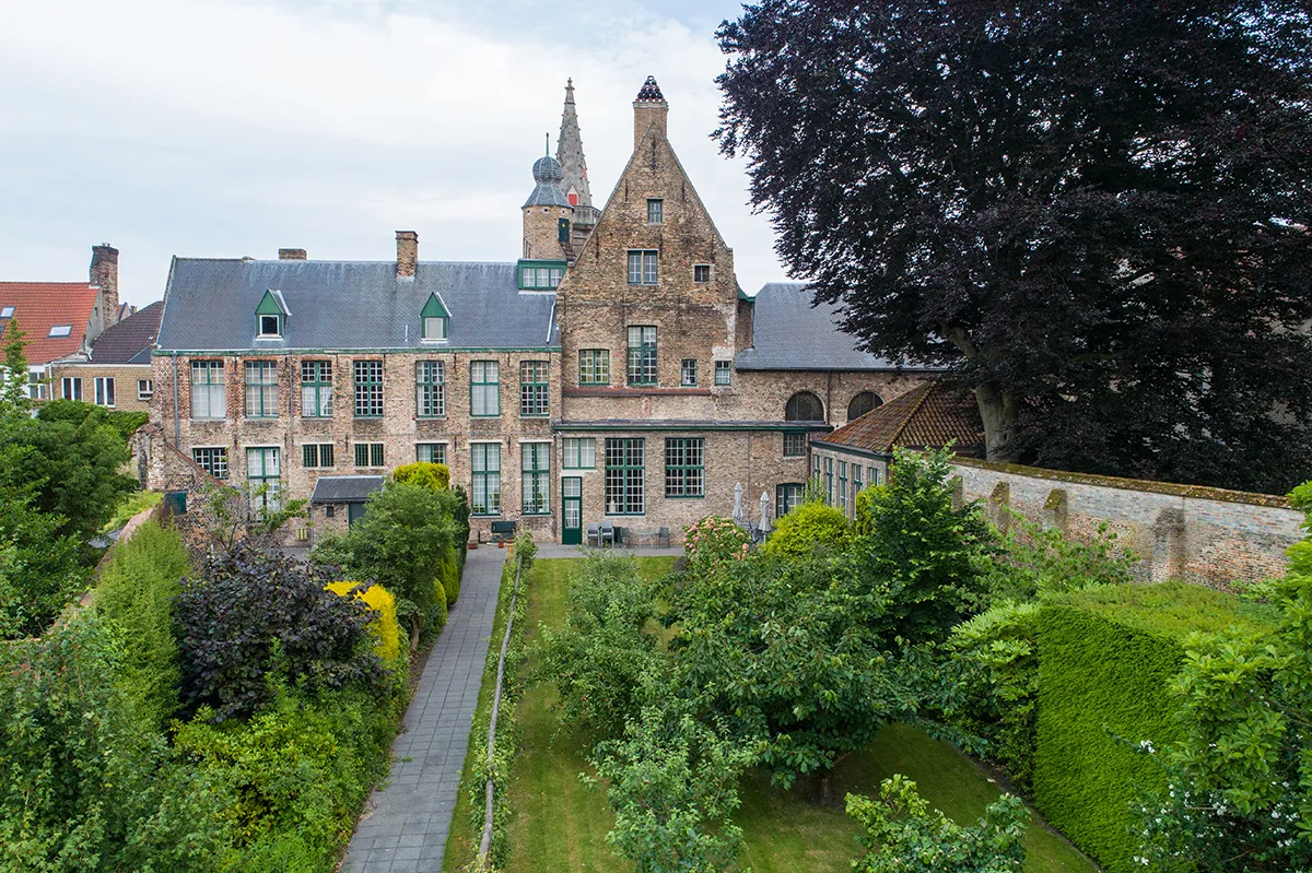 Vista exterior de Hof Bladelin que muestra el histórico edificio de ladrillo con fachadas escalonadas y un jardín interior cerrado con setos y un camino central.
