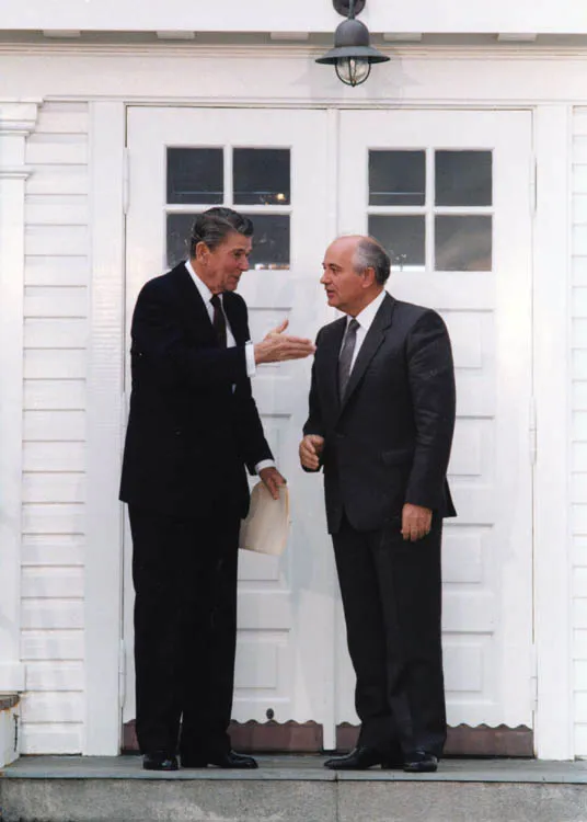 Two men in dark suits conversing in front of the white double doors and clapboard facade of Höfði House in Reykjavík