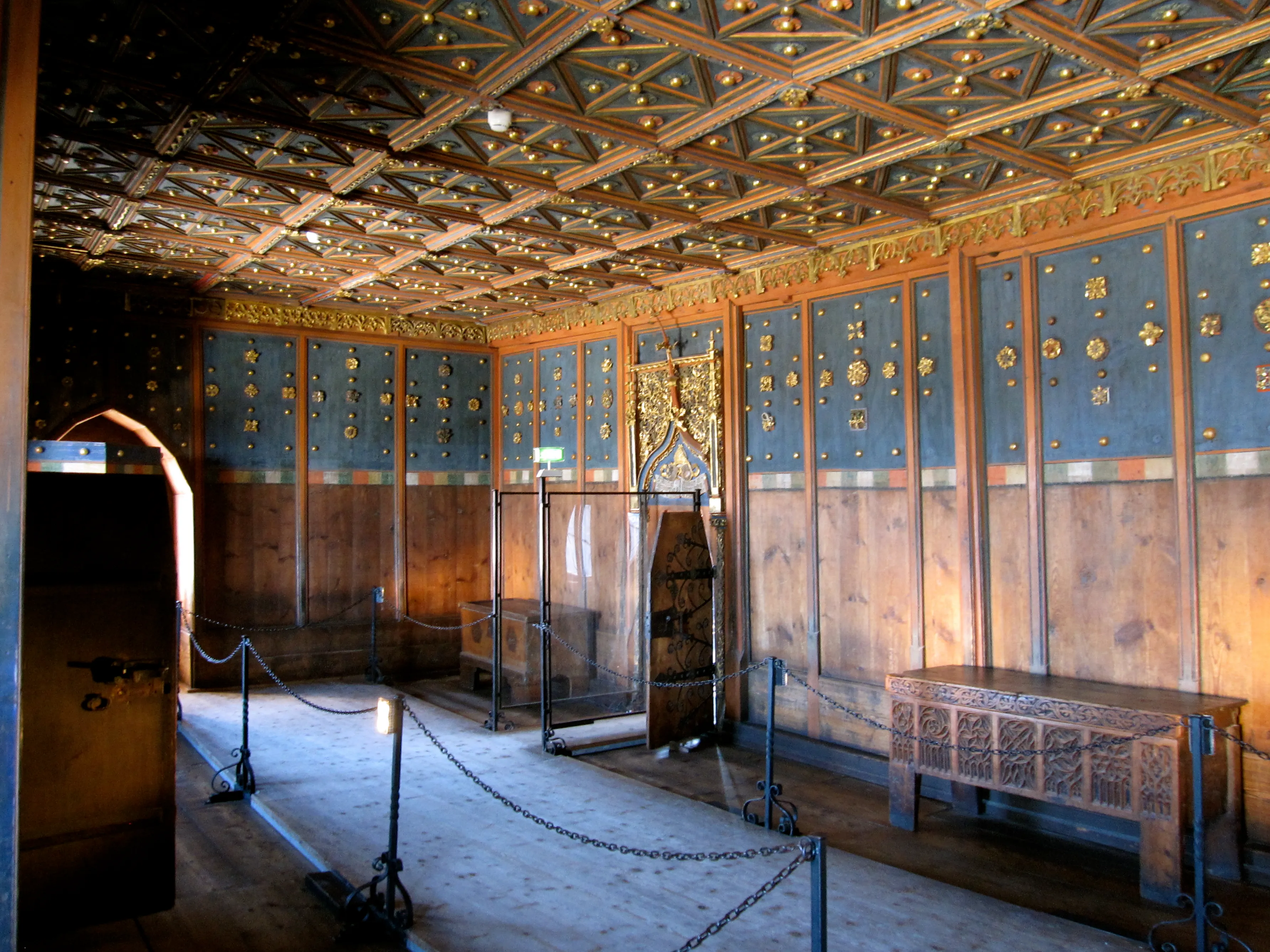 Sala histórica ornamentada con techo artesonado dorado, paredes con paneles azules y decoraciones en oro, arca de madera y vitrinas de cristal dentro de la fortaleza de Hohensalzburg