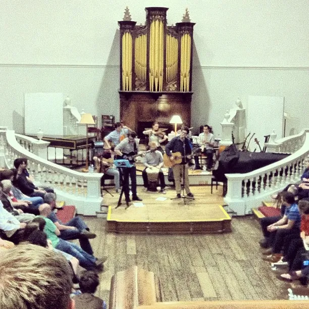 Interieur van de Holywell Music Room met musici op een houten podium, het publiek aan weerszijden gezeten en een groot pijporgel aan de achterwand.
