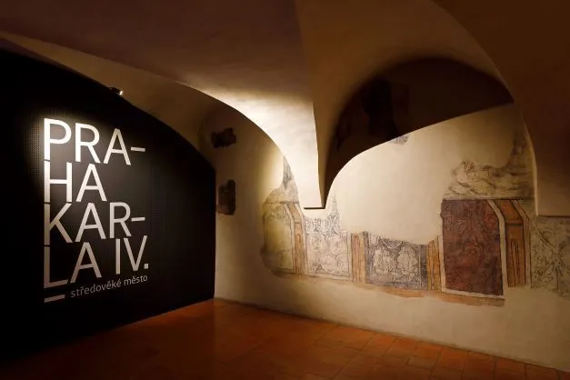 Galería interior con techo abovedado, un letrero iluminado que dice 'PRAHA KARLA IV.' y murales históricos en la pared