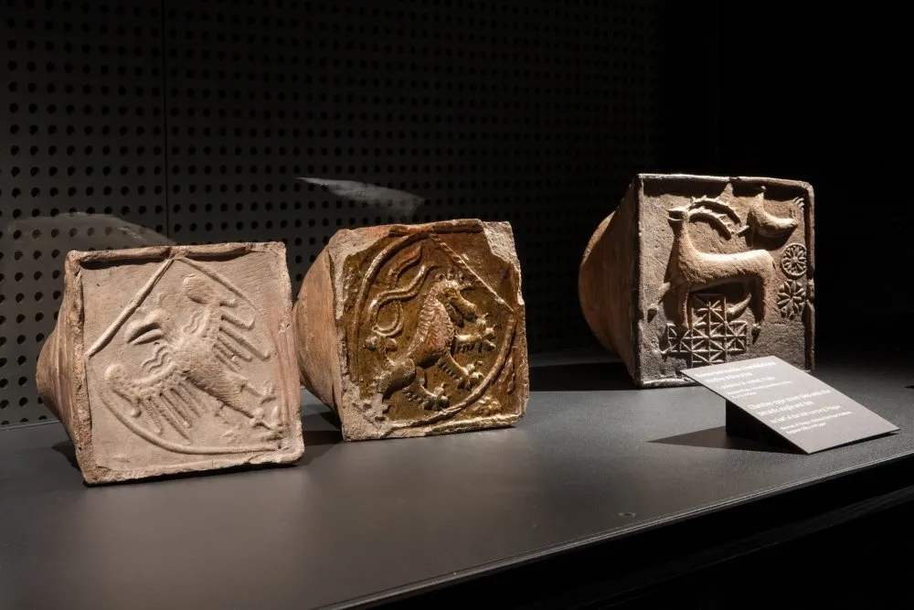 Tres azulejos de piedra tallada con símbolos heráldicos en exhibición en un museo