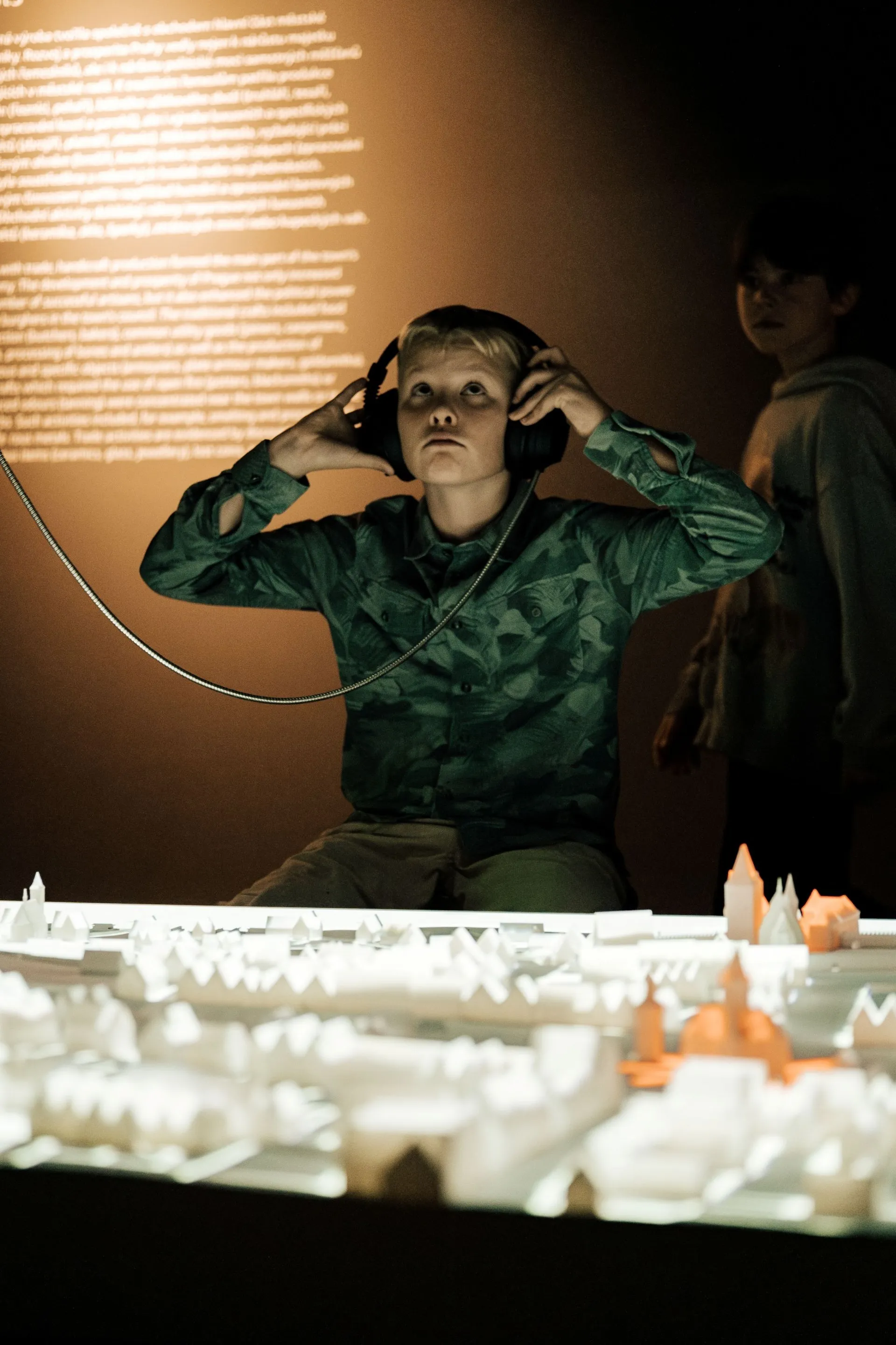 Un chico con auriculares interactúa con una maqueta de edificios de Praga en una exposición.