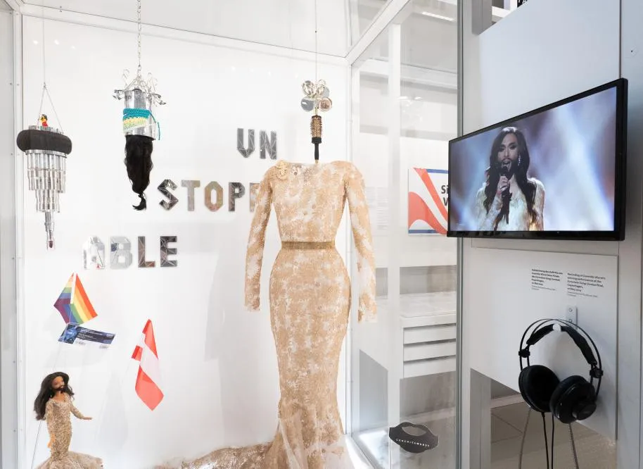 exhibition with a beige lace dress, a TV screen, headphones, and hanging objects