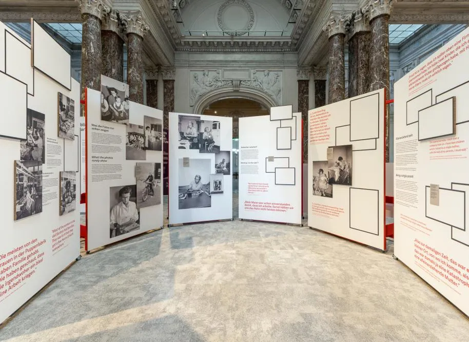 Exhibition panels with historical photos and text in a grand hall with marble columns